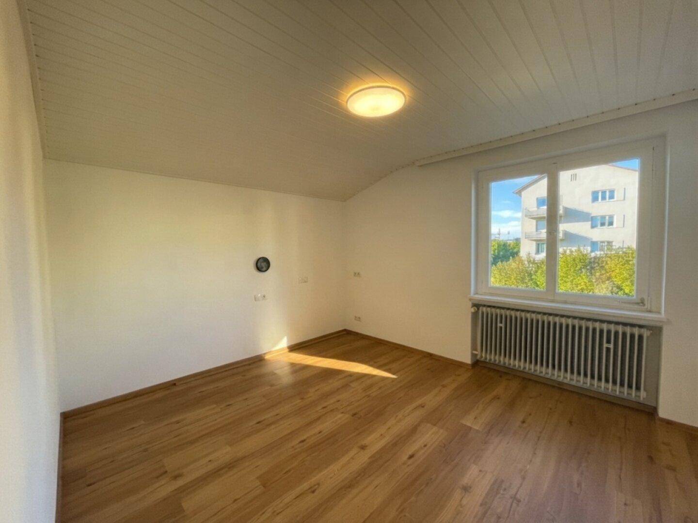 Helles Zimmer mit Laminatboden, weißen Wänden und einem großen Fenster.