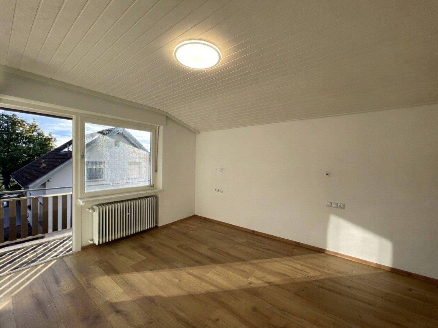 Freundliches Zimmer mit Laminatboden, Fenster und Zugang zu einem Außenbereich.
