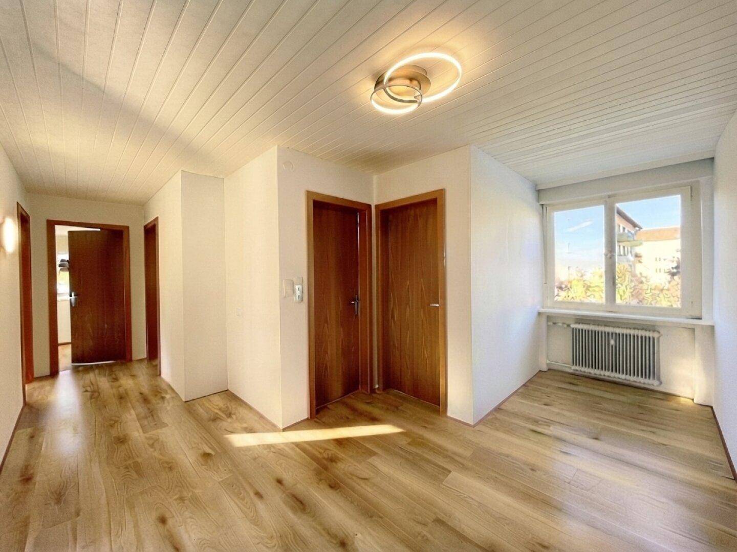 Heller Flur mit Laminatboden, weißen Wänden und mehreren Holztüren.