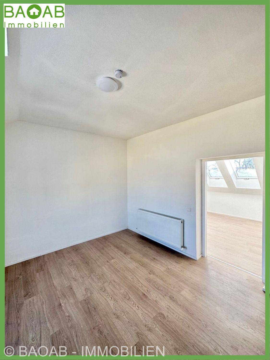 Ruhiges Zimmer mit Holzfußboden und weiß gestrichenen Wänden, bereit zur individuellen Gestaltung.