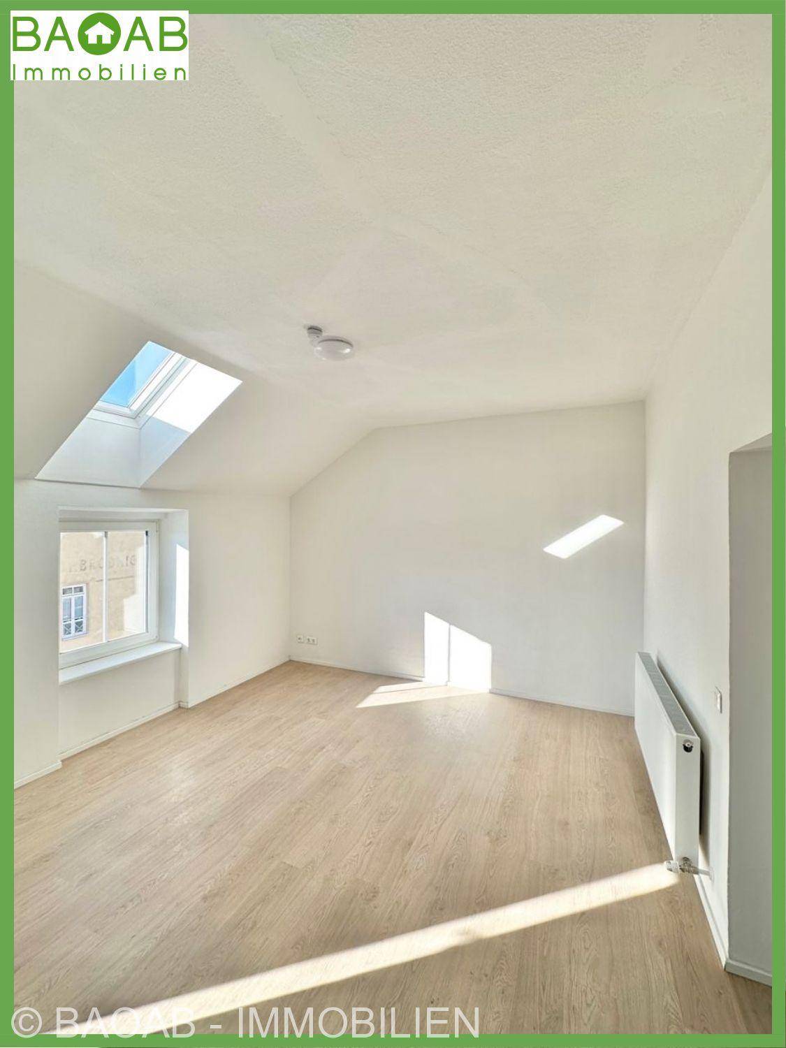 Lichtdurchfluteter Raum mit Dachschräge, Holzfußboden und einem großen Dachfenster für viel Tageslicht.