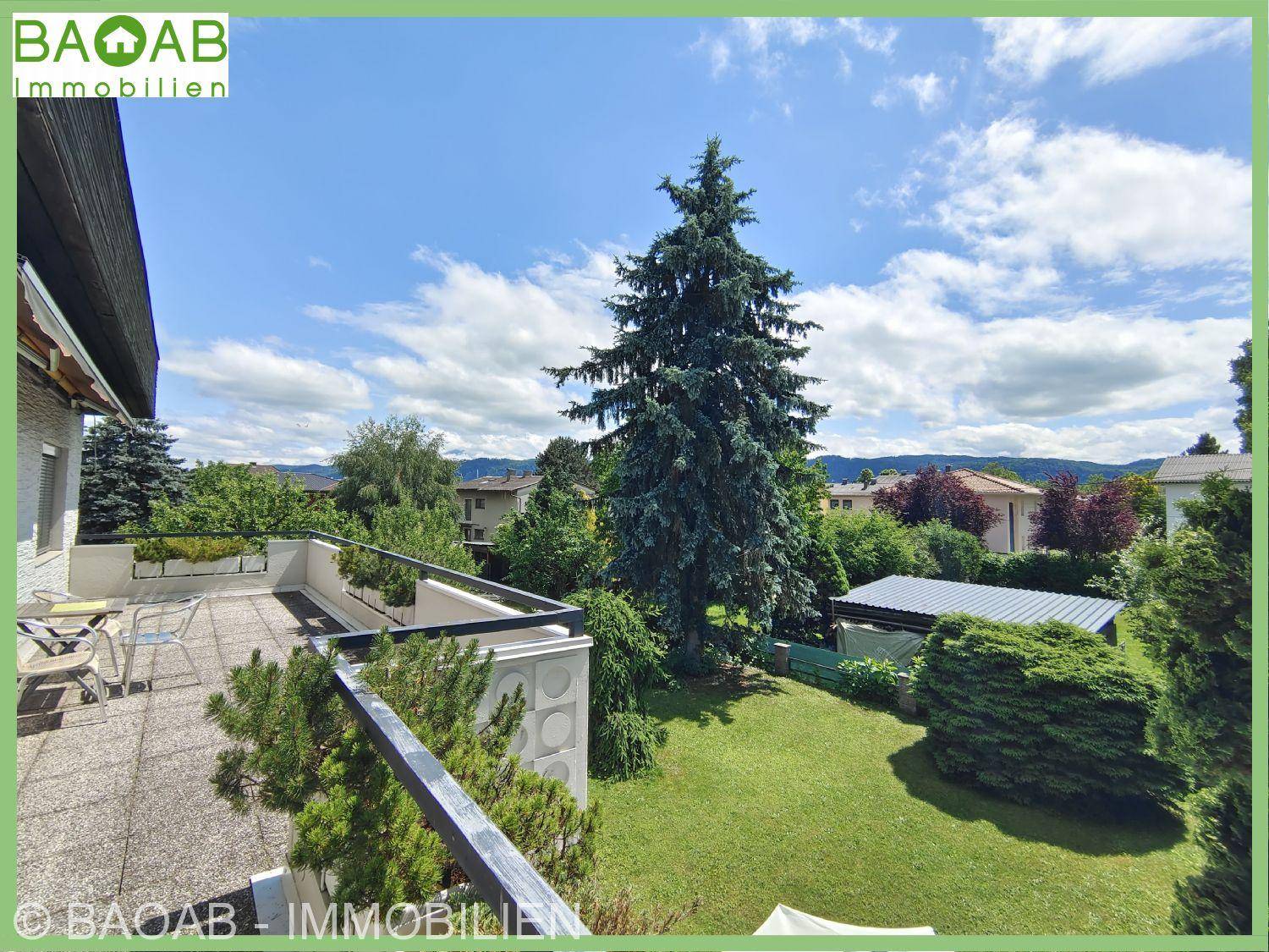 Geräumige Terrasse mit Fliesenboden und Blick auf den weitläufigen grünen Garten mit hohen Bäumen.