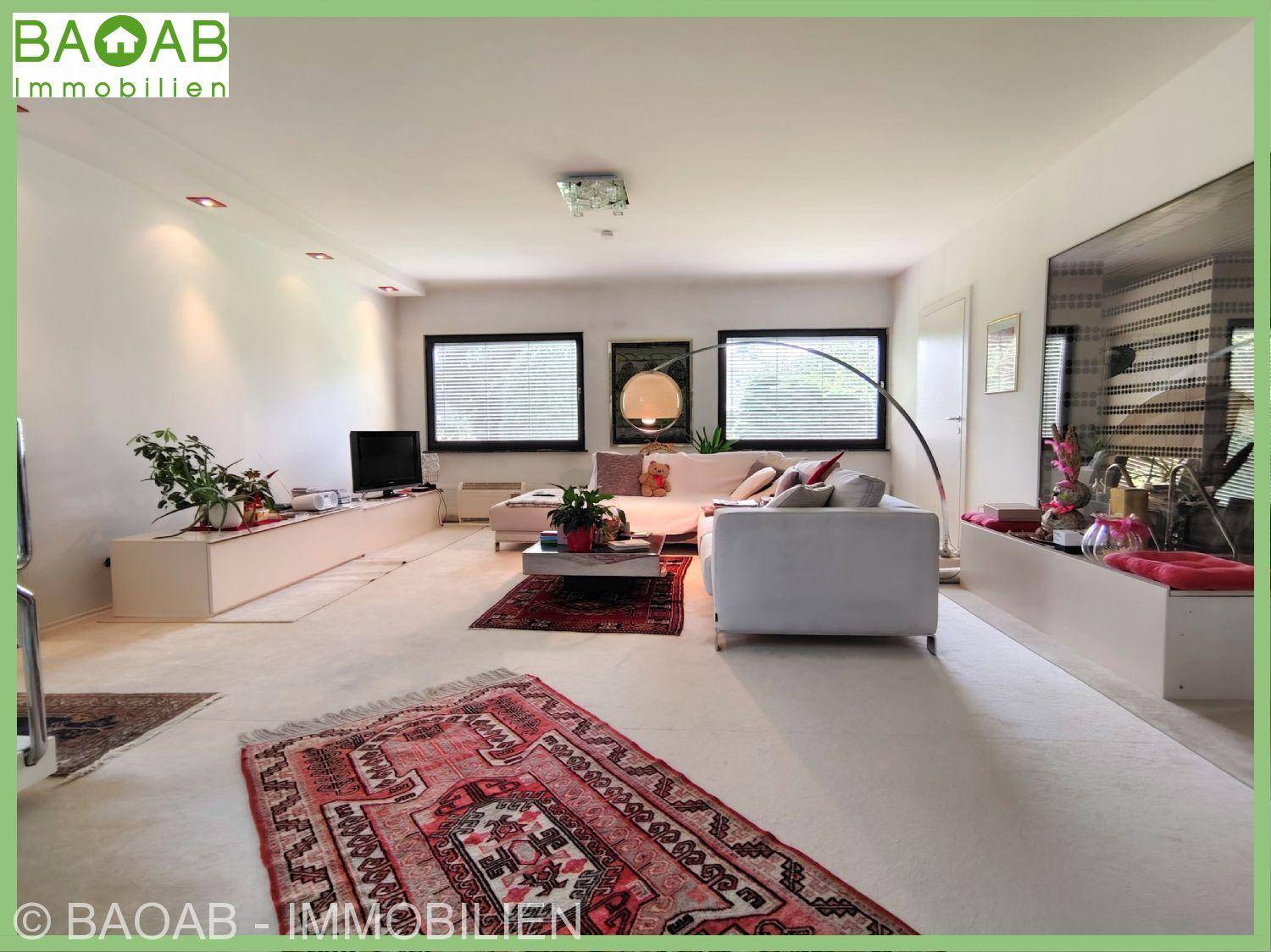 Helles Wohnzimmer mit bequemen weißen Sofas, Teppichboden und großen Fenstern für viel Tageslicht.