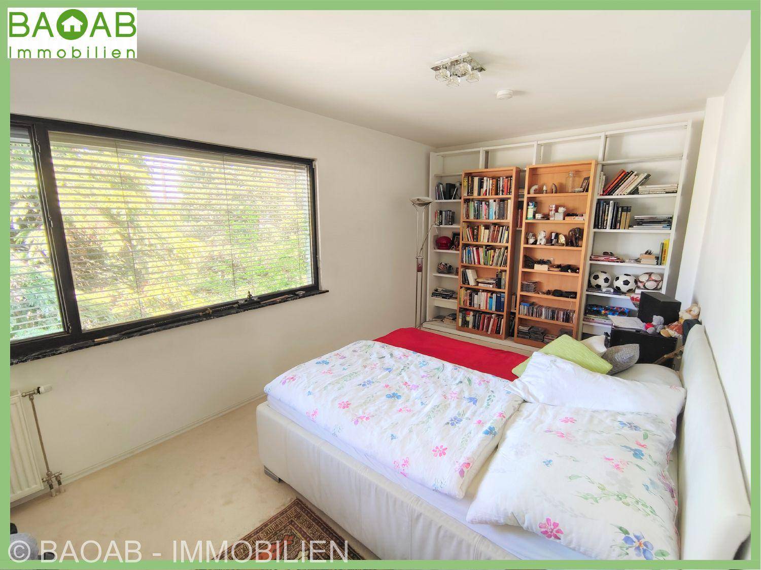 Helles Schlafzimmer mit Bett, integrierten Bücherregalen und großem Fenster mit Blick ins Grüne.