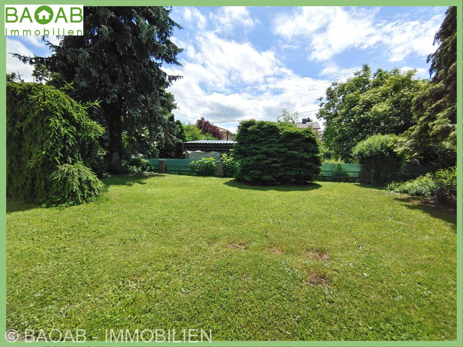 Weitläufiger grüner Garten mit altem Baumbestand und gepflegtem Rasen unter blauem Himmel.