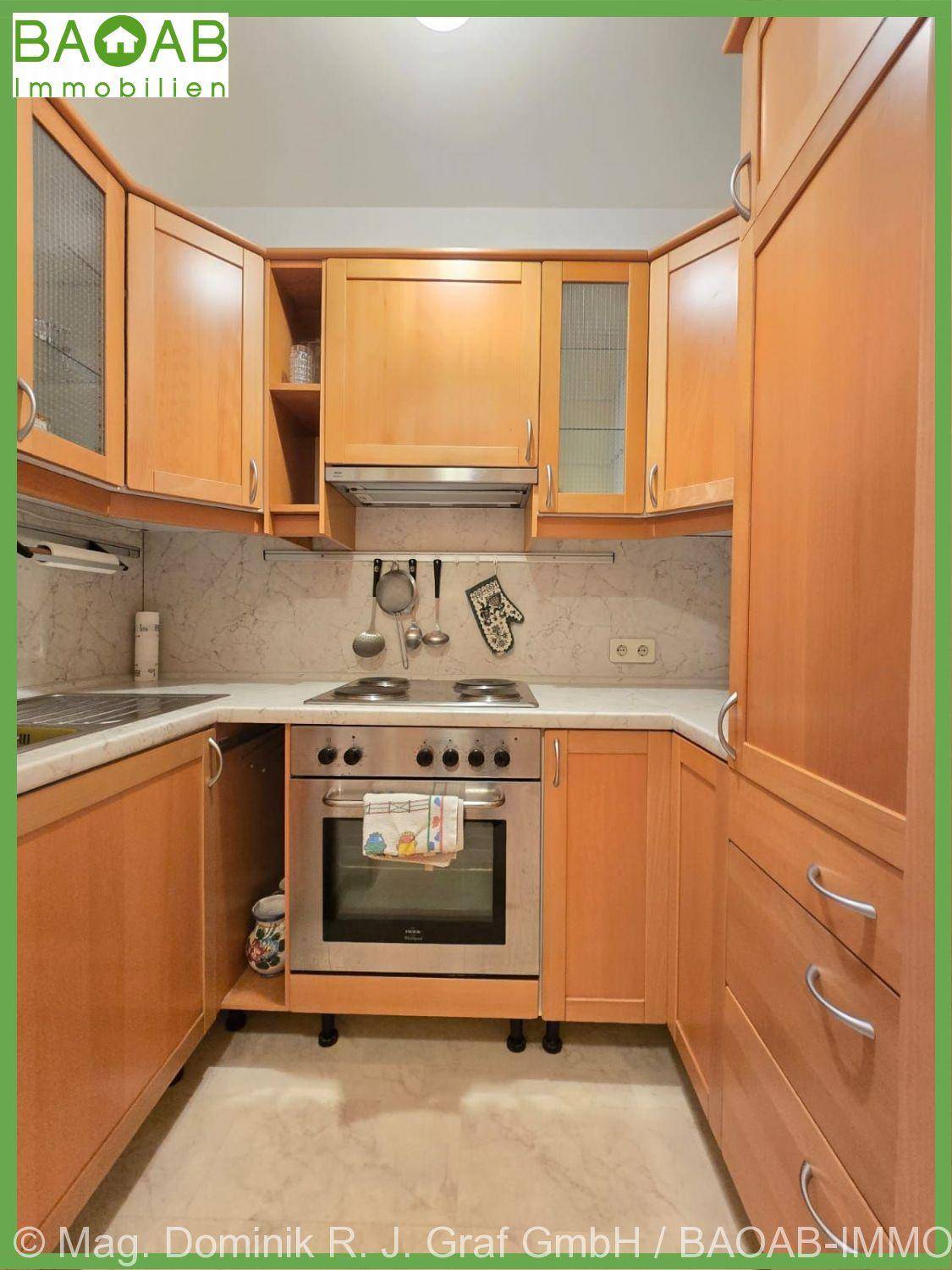 Funktionale Küche mit Holzschränken, integriertem Backofen und ausreichend Arbeitsfläche.