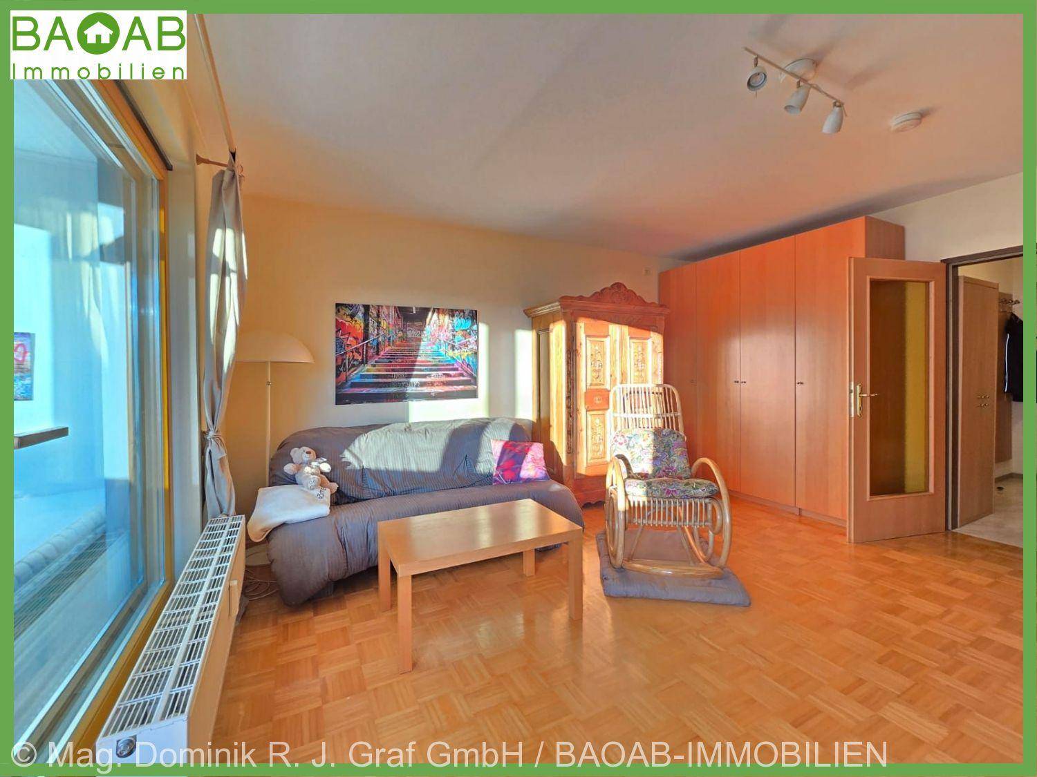 Wohnzimmer mit Parkettboden, bequemer Couch und großem Schrank, bietet Zugang zu einem verglasten Balkon.