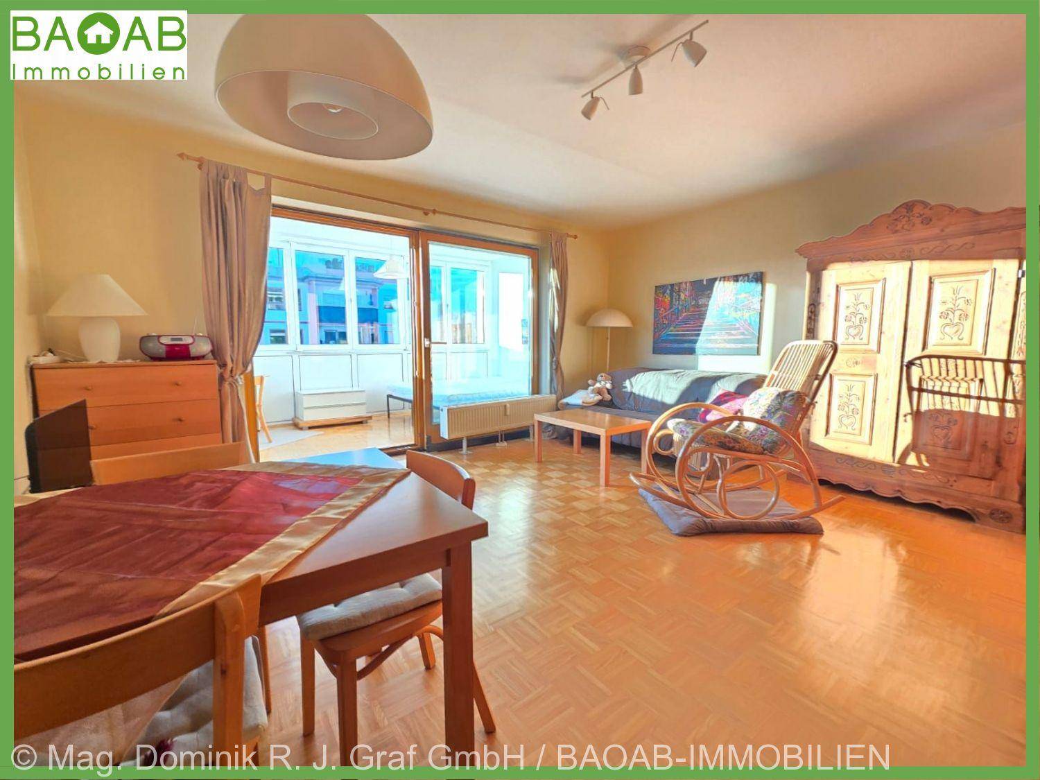 Gemütlicher Wohn-Essbereich mit Parkettboden, traditionellen Möbeln und Zugang zu einem verglasten Balkon.