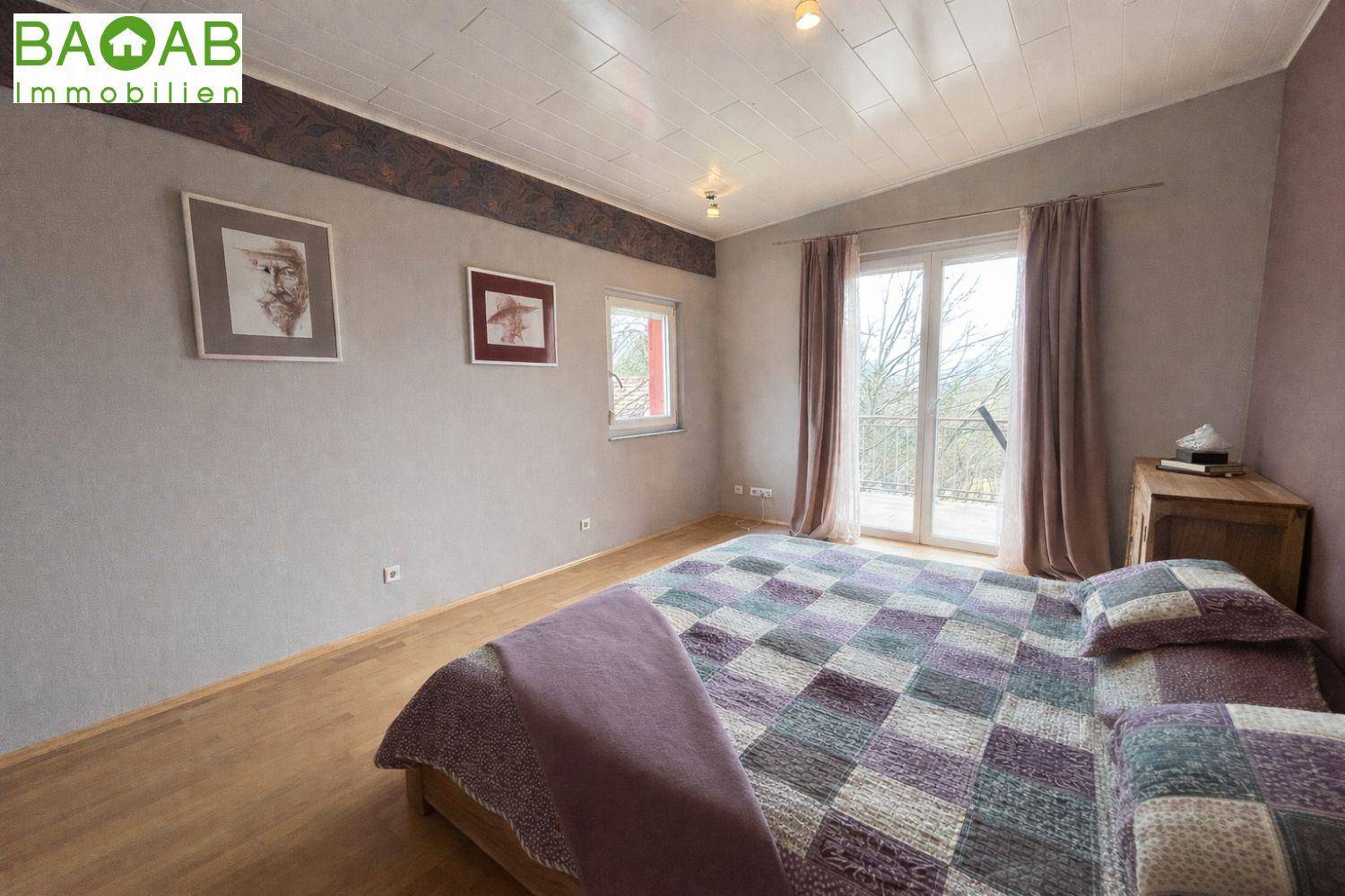 Schlafzimmer mit Holzboden, Zugang zum Balkon und Blick auf die umliegende Landschaft.