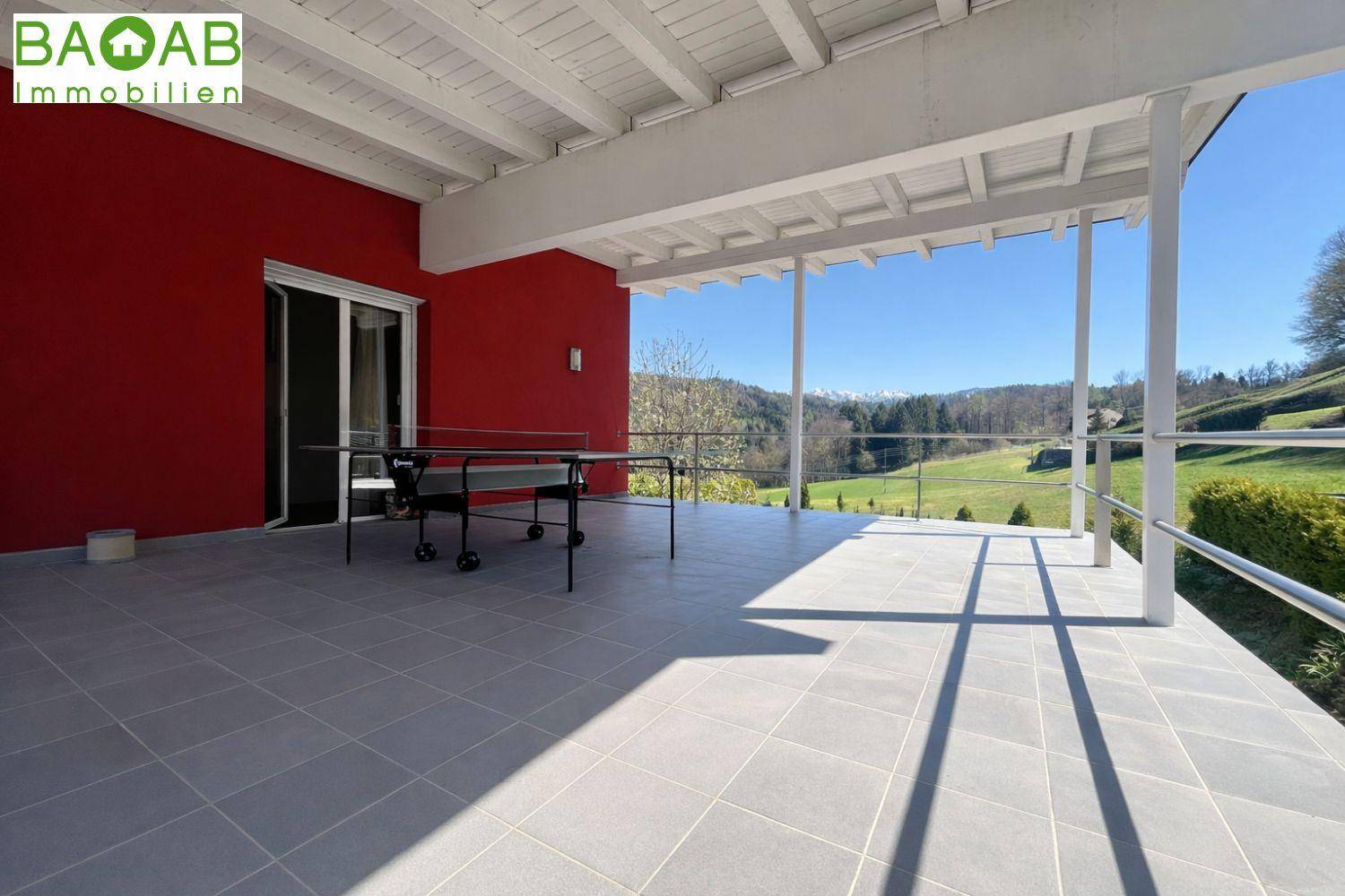 Große überdachte Terrasse mit Fliesenboden und weitem Blick über die grüne Landschaft.