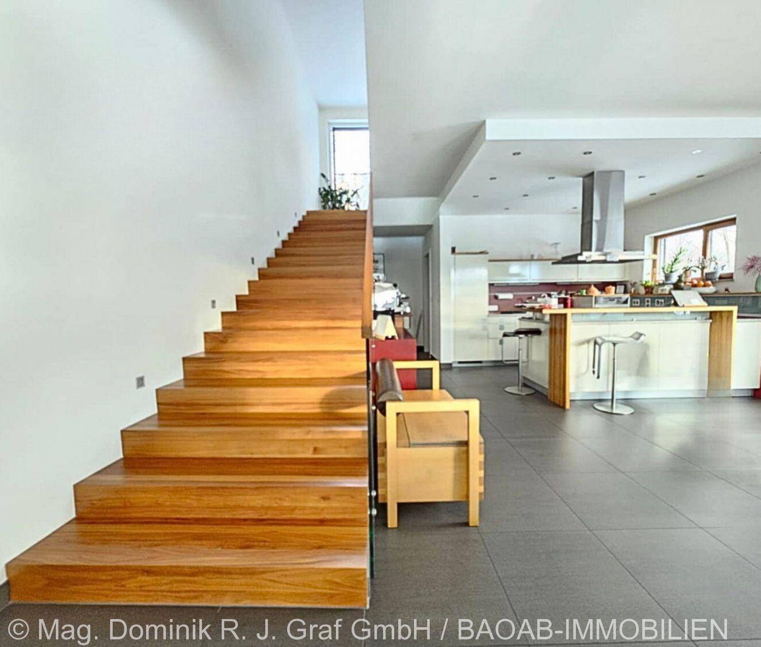 Helle Holztreppe führt in die obere Etage, mit offenem Blick auf die moderne Küche.