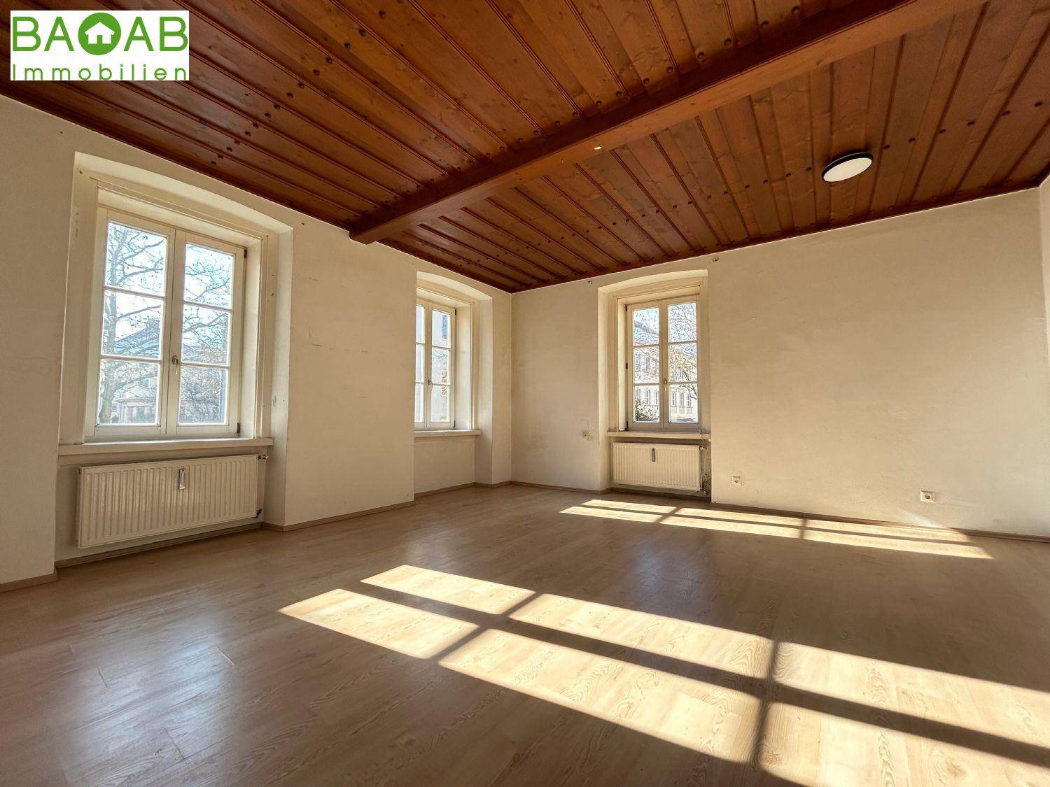 Geräumiges Zimmer mit Holzbalkendecke, hellem Holzboden und viel natürlichem Sonnenlicht.
