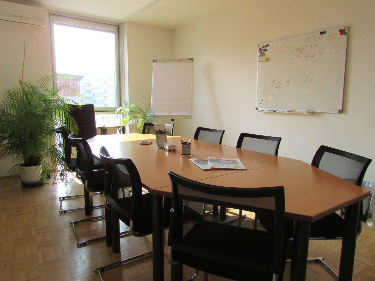 Konferenzraum mit großem ovalen Tisch, bequemen Stühlen, Whiteboard und einem Fenster für natürliches Licht.