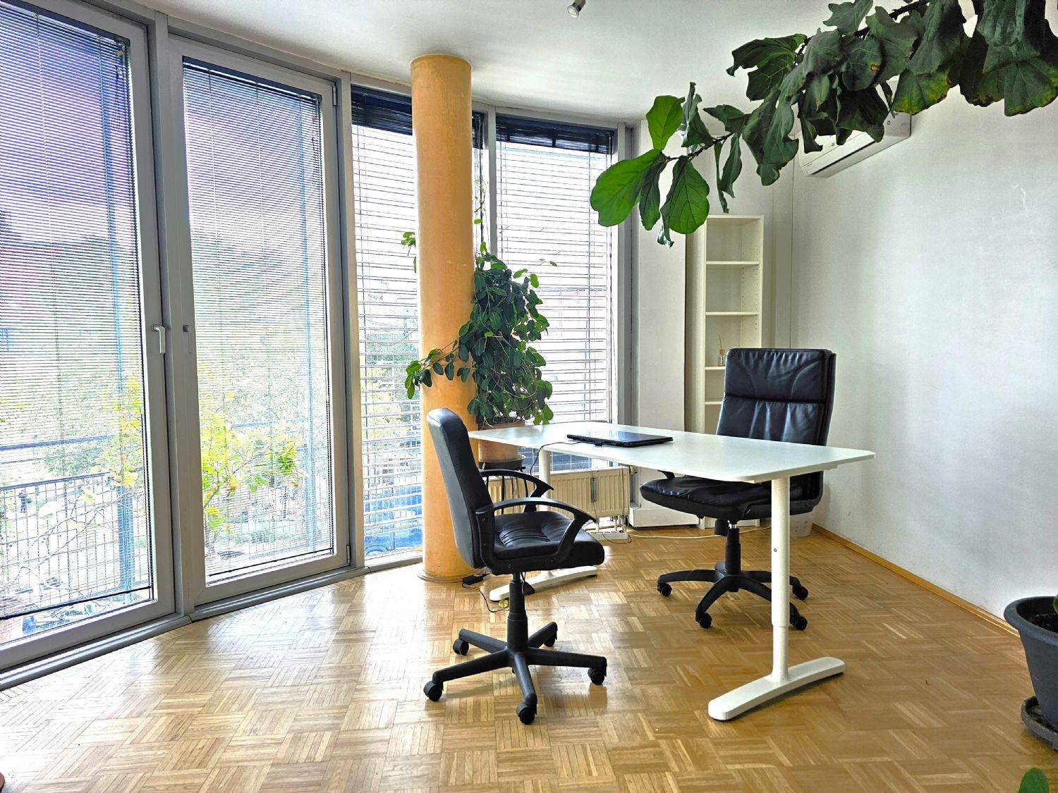 Modernes Büro mit großen Fenstern, die auf einen Balkon führen, ausgestattet mit Schreibtisch und Bürostühlen.