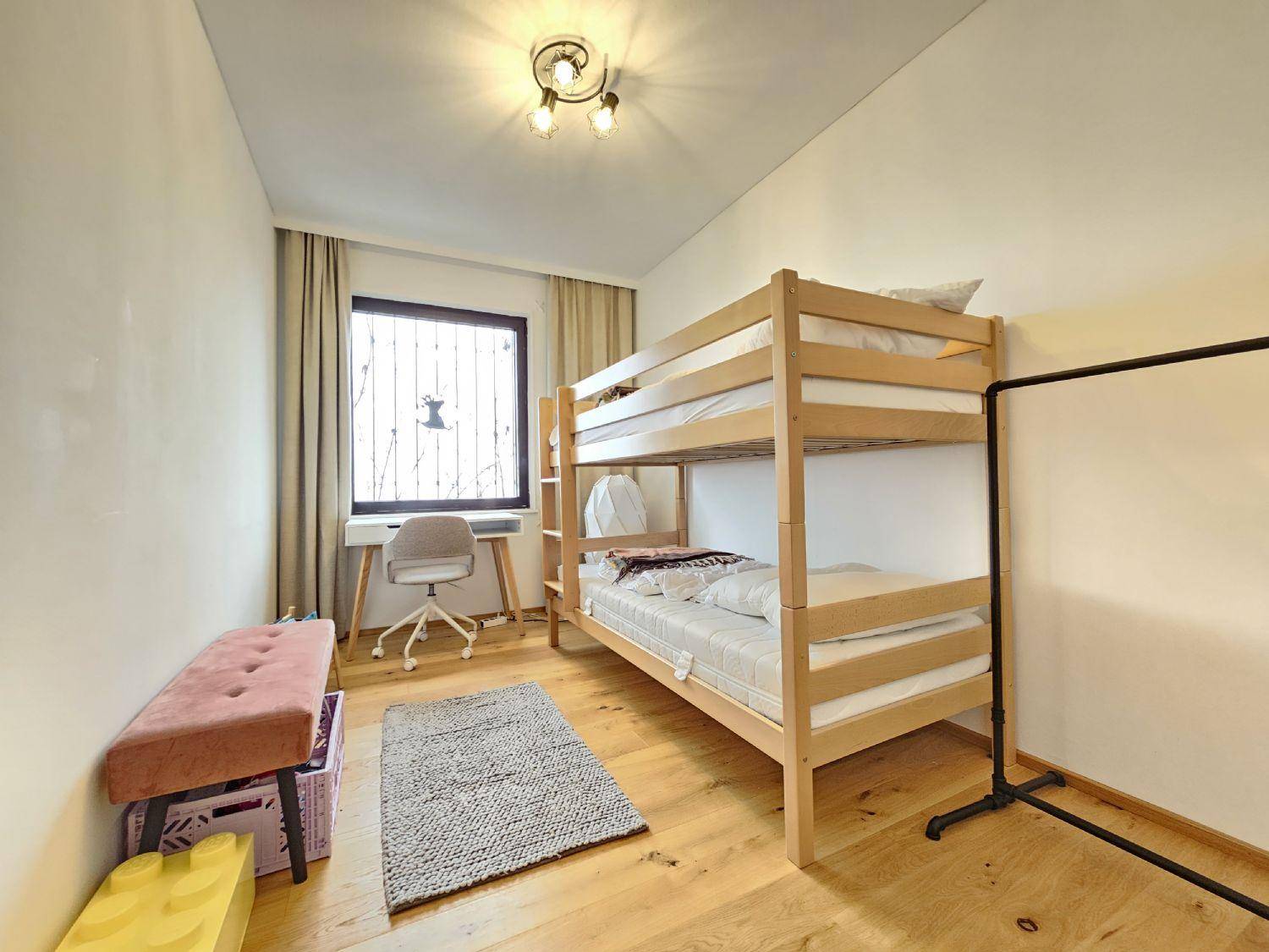 Kinderzimmer mit Etagenbett aus Holz, Schreibtisch und einem Fenster für natürliches Licht.