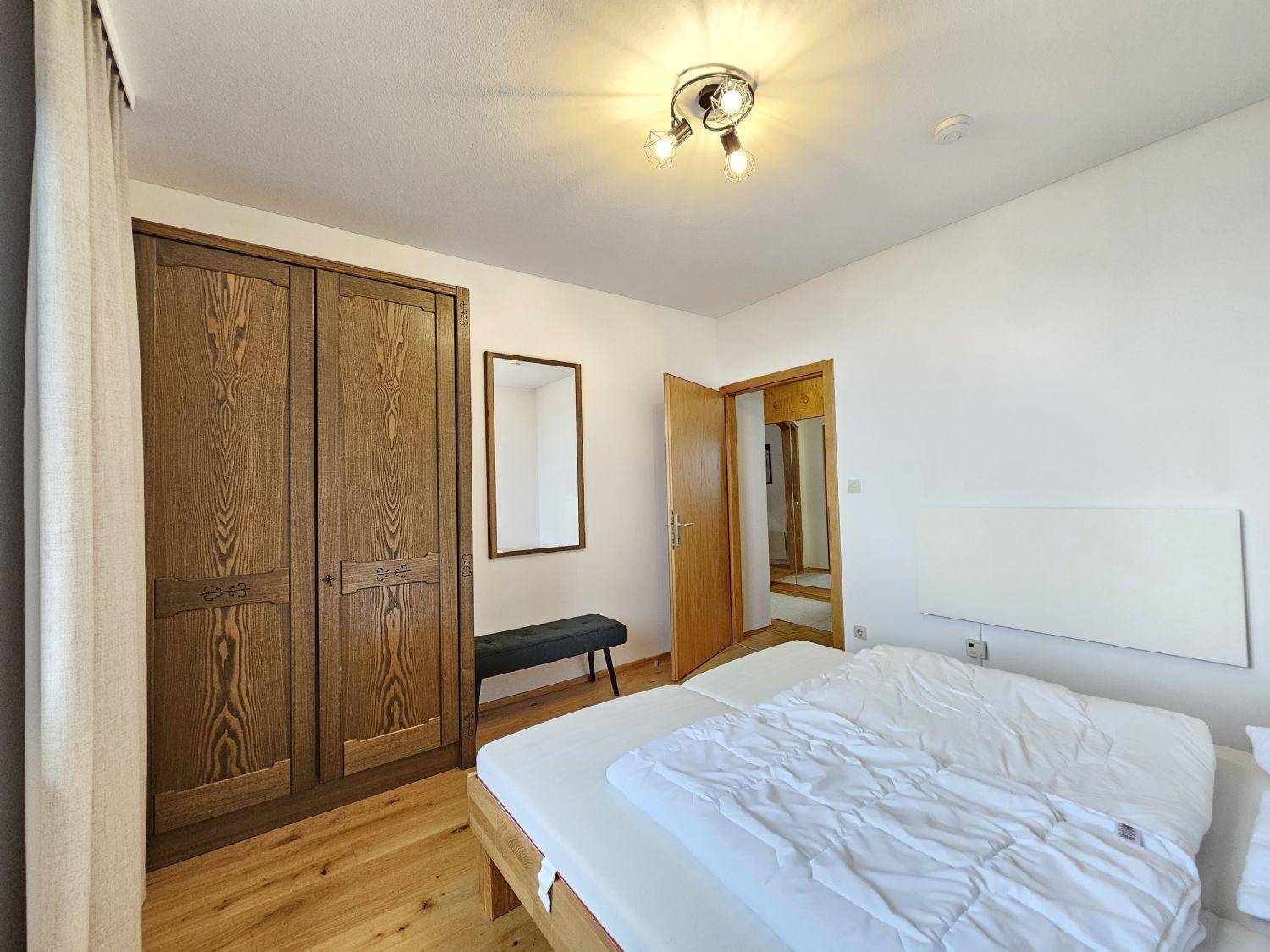 Helles Schlafzimmer mit Holzbett, großem Kleiderschrank und einem Spiegel an der Wand.