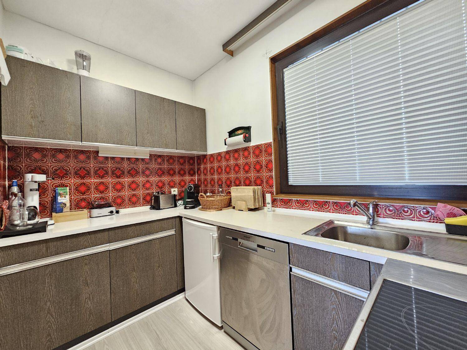 Funktionale Küche mit Holzschränken, Spülmaschine und einem Fenster mit Jalousien.