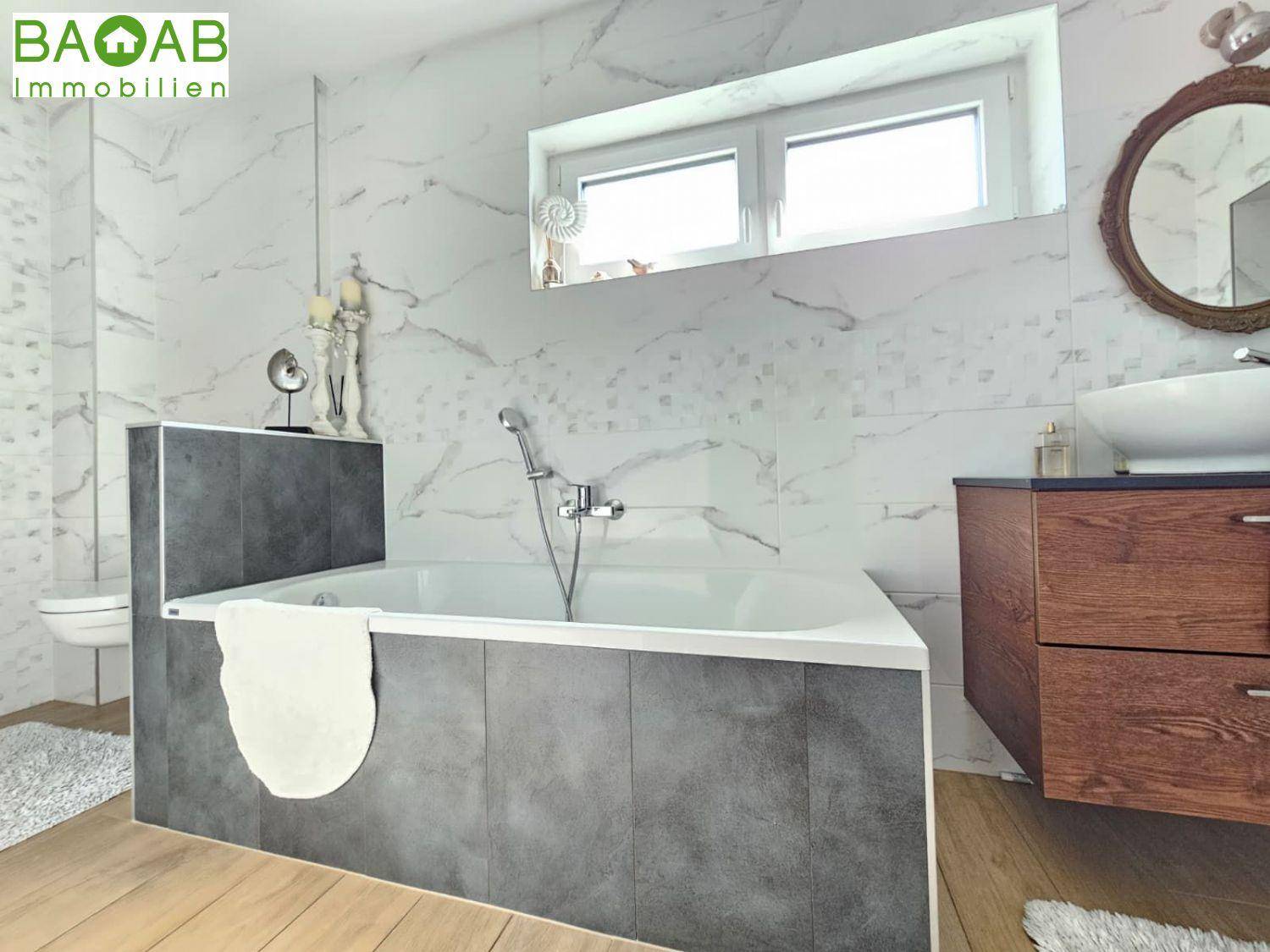 Modernes Badezimmer mit Badewanne, Marmoroptik-Fliesen und Fenster für Tageslicht.