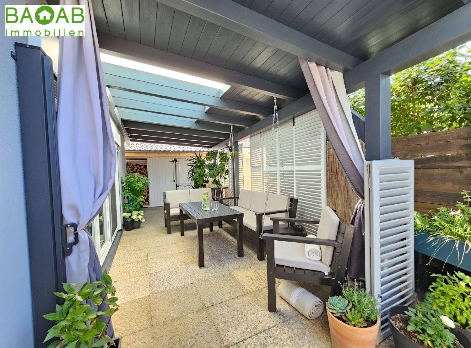 Überdachte Terrasse mit gemütlicher Sitzecke, Pflanzen und Sichtschutz.