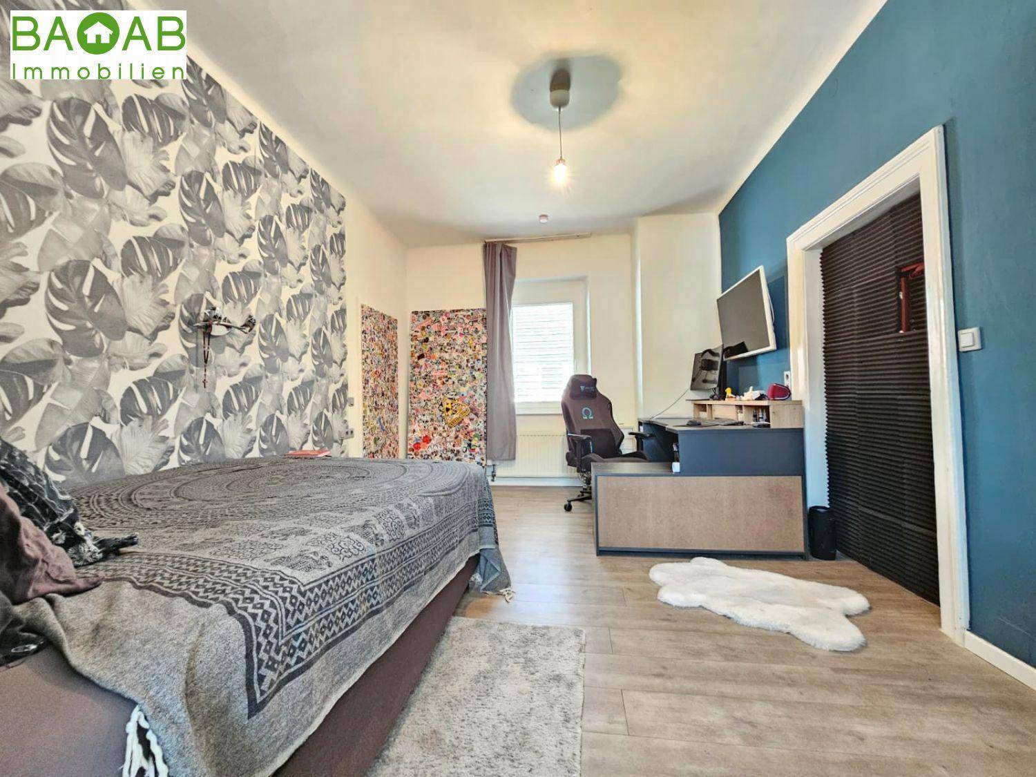 Modernes Schlafzimmer mit auffälliger Tapete, Holzboden und integriertem Arbeitsbereich.