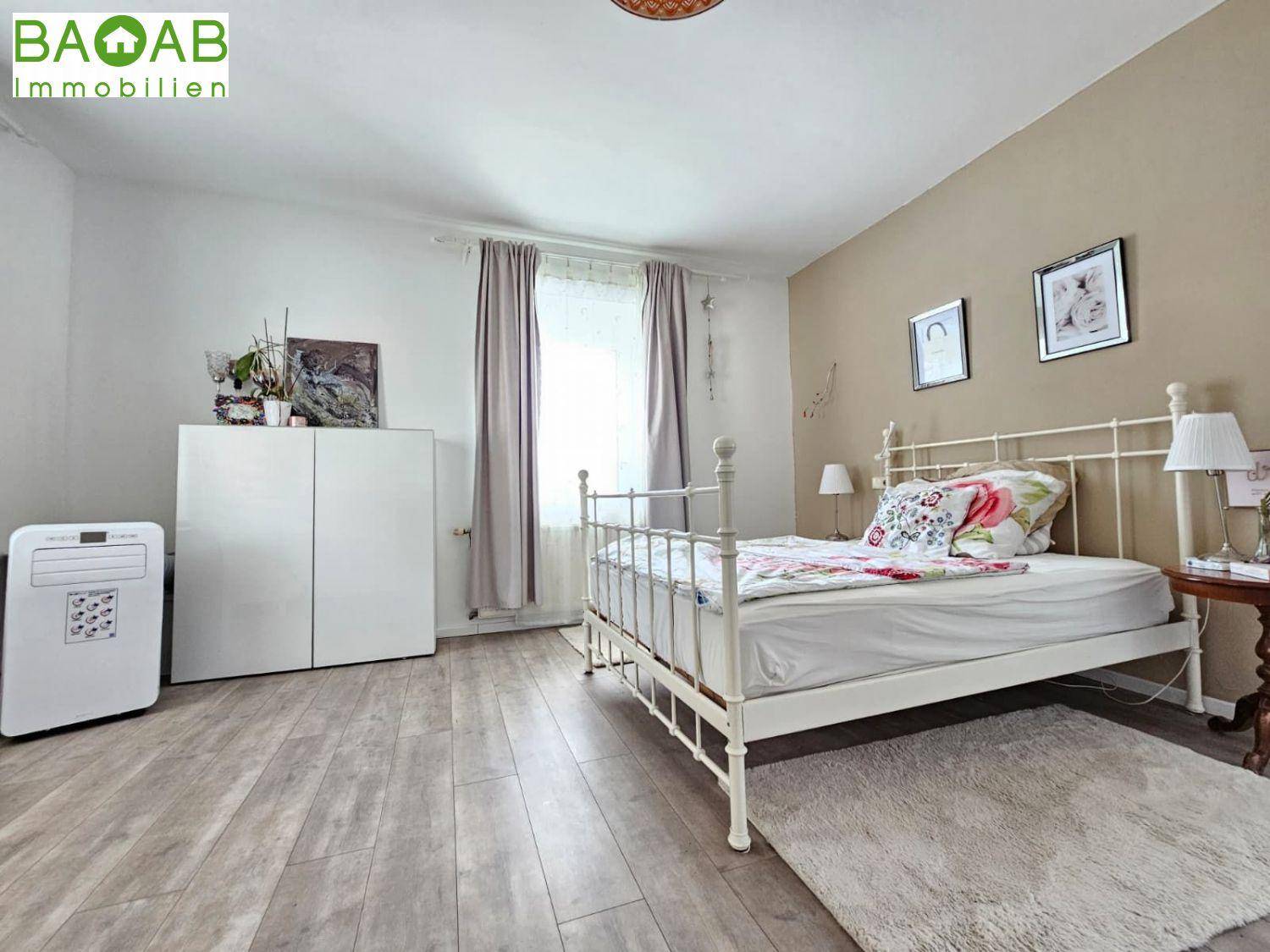 Helles Schlafzimmer mit hellem Holzboden, weißem Metallbett und Klimaanlage.