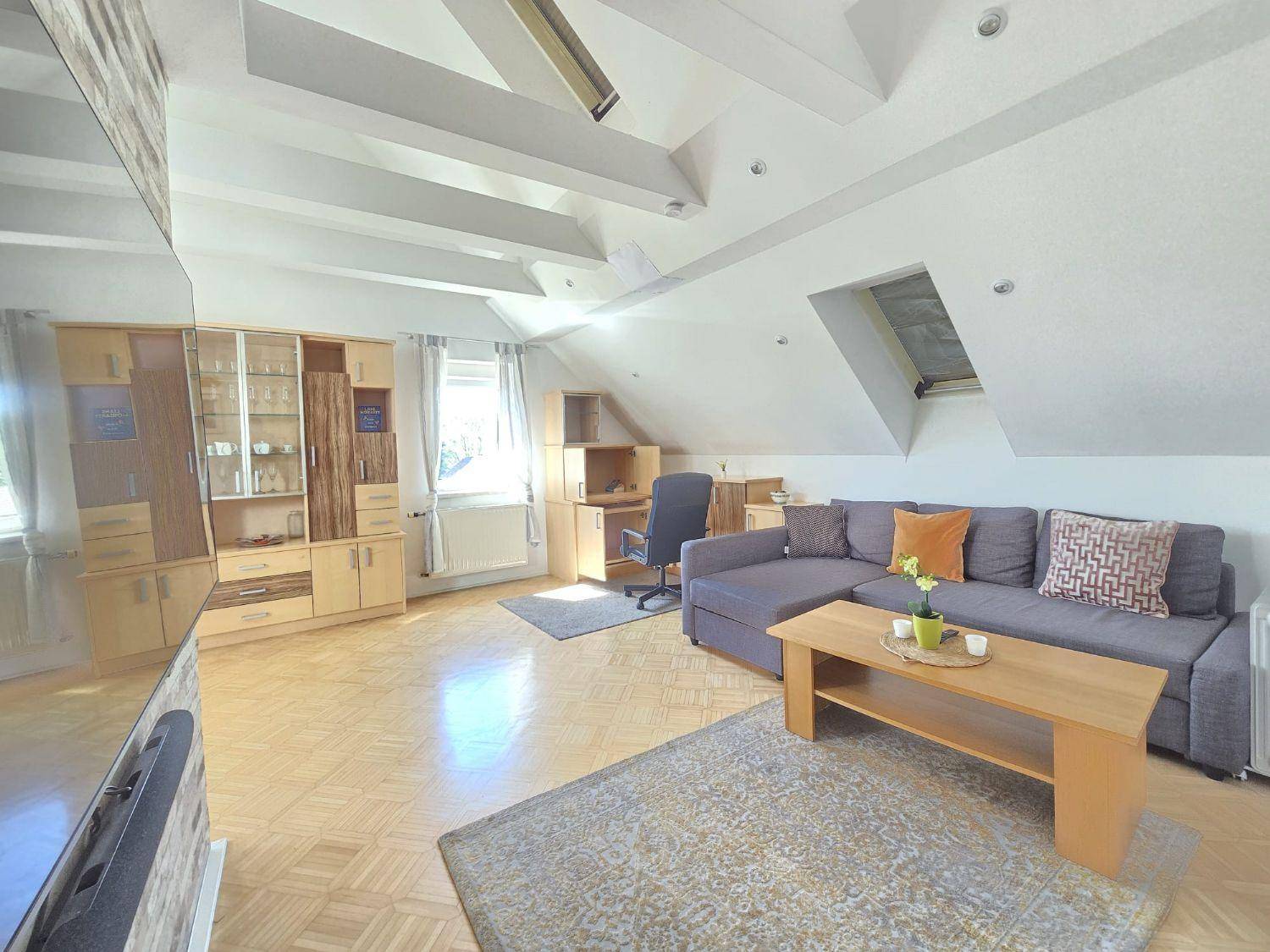 Geräumiges Wohnzimmer mit großem Sofa, Couchtisch und Dachschrägen mit Oberlichtern.