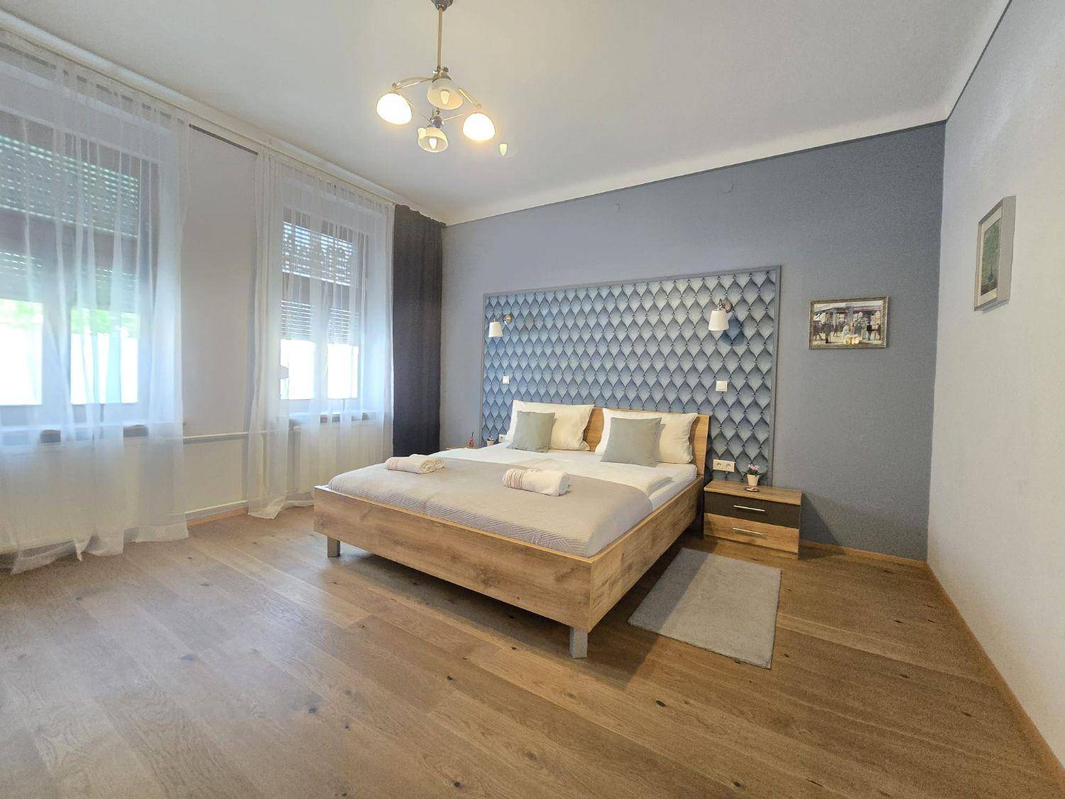 Helles Schlafzimmer mit breiten Holzplanken, dekorativem Kopfteil und großen Fenstern.