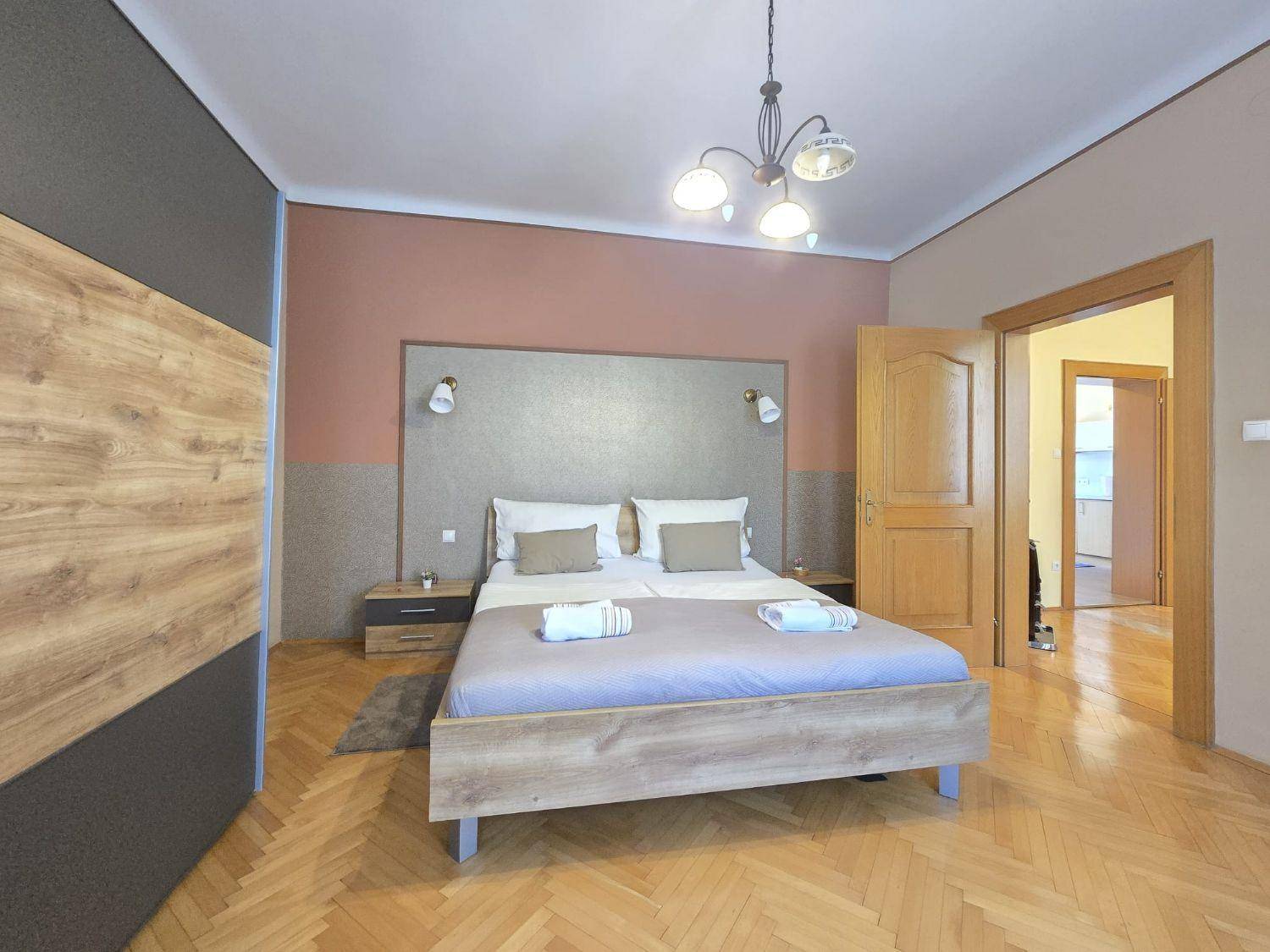 Gemütliches Schlafzimmer mit Doppelbett, Fischgrätparkett und Zugang zu einem weiteren Raum.