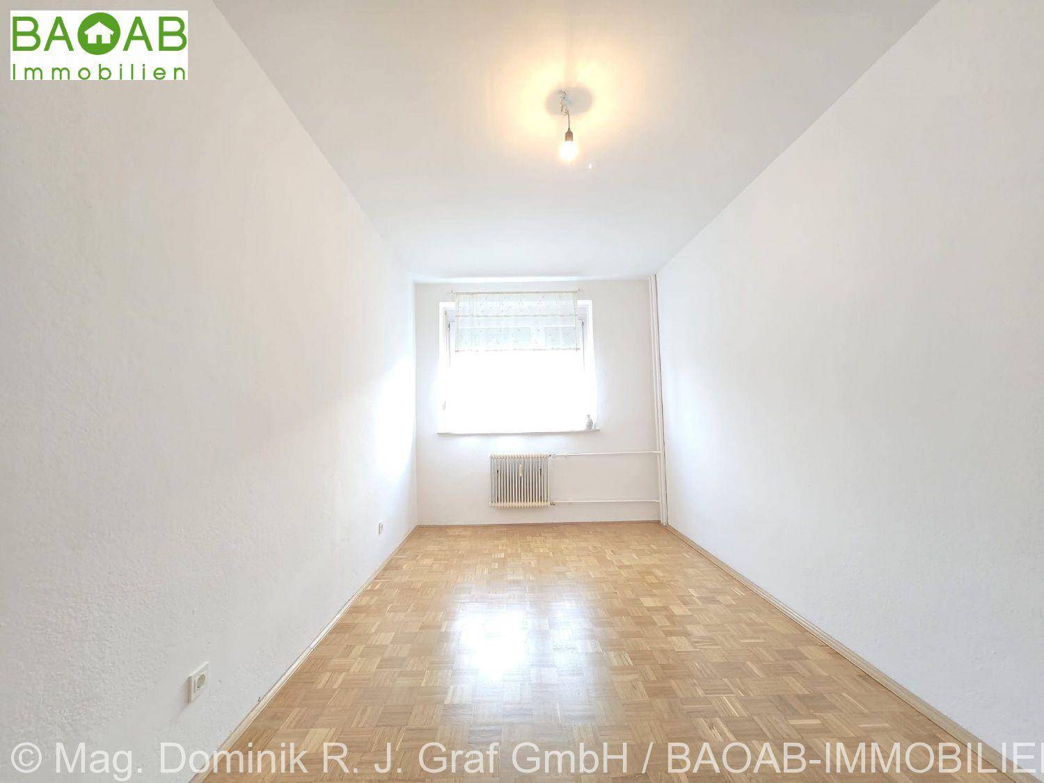 Leeres Zimmer mit Parkettboden und Fenster, bereit zur individuellen Gestaltung und Nutzung.
