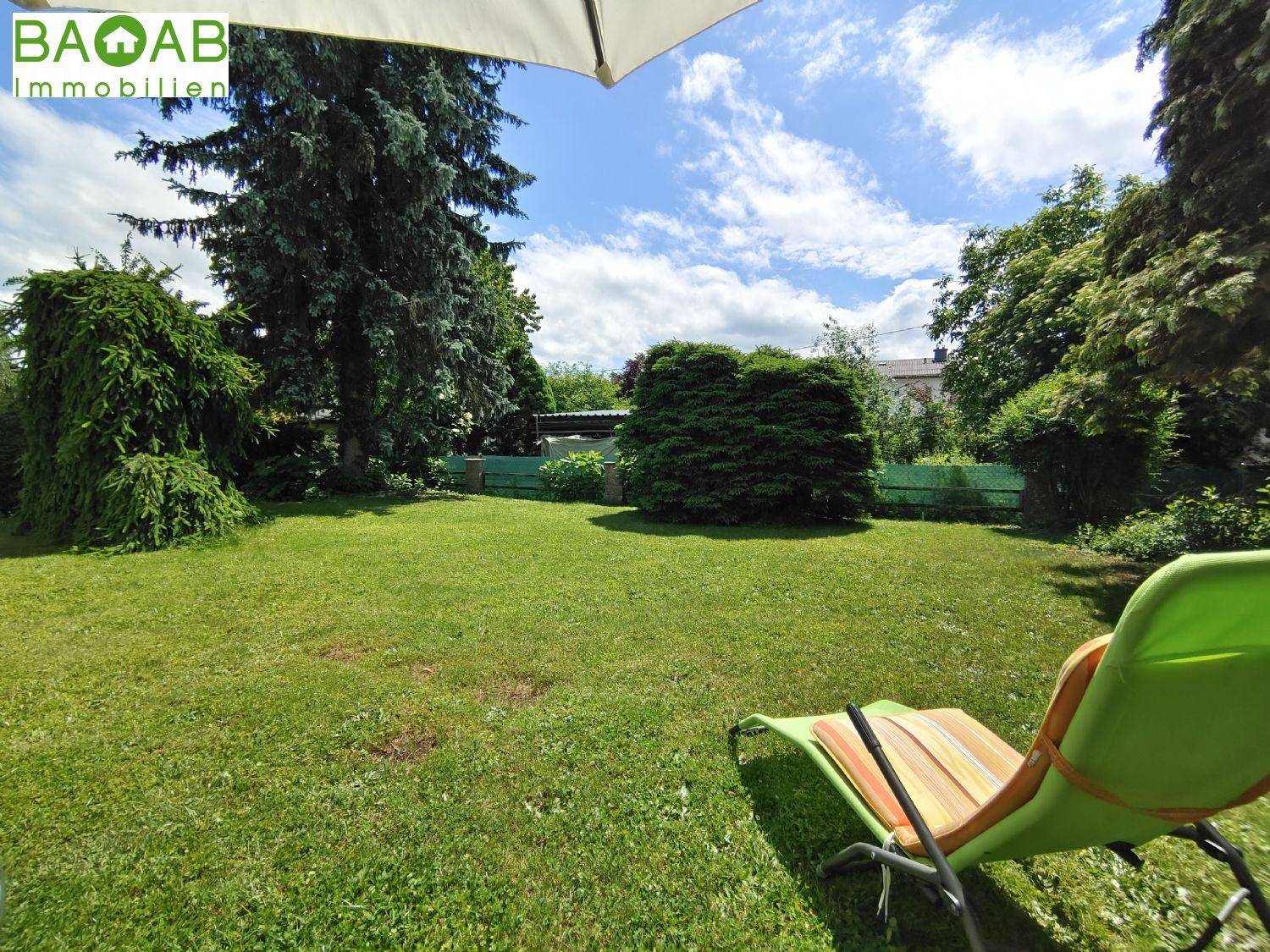 Weitläufiger Garten mit großer Rasenfläche und einem Liegestuhl zum Entspannen im Freien.