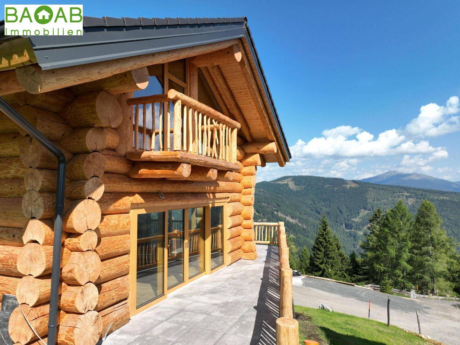 Außenansicht eines Holzchalets mit Balkon und Terrasse vor einer beeindruckenden Bergkulisse.