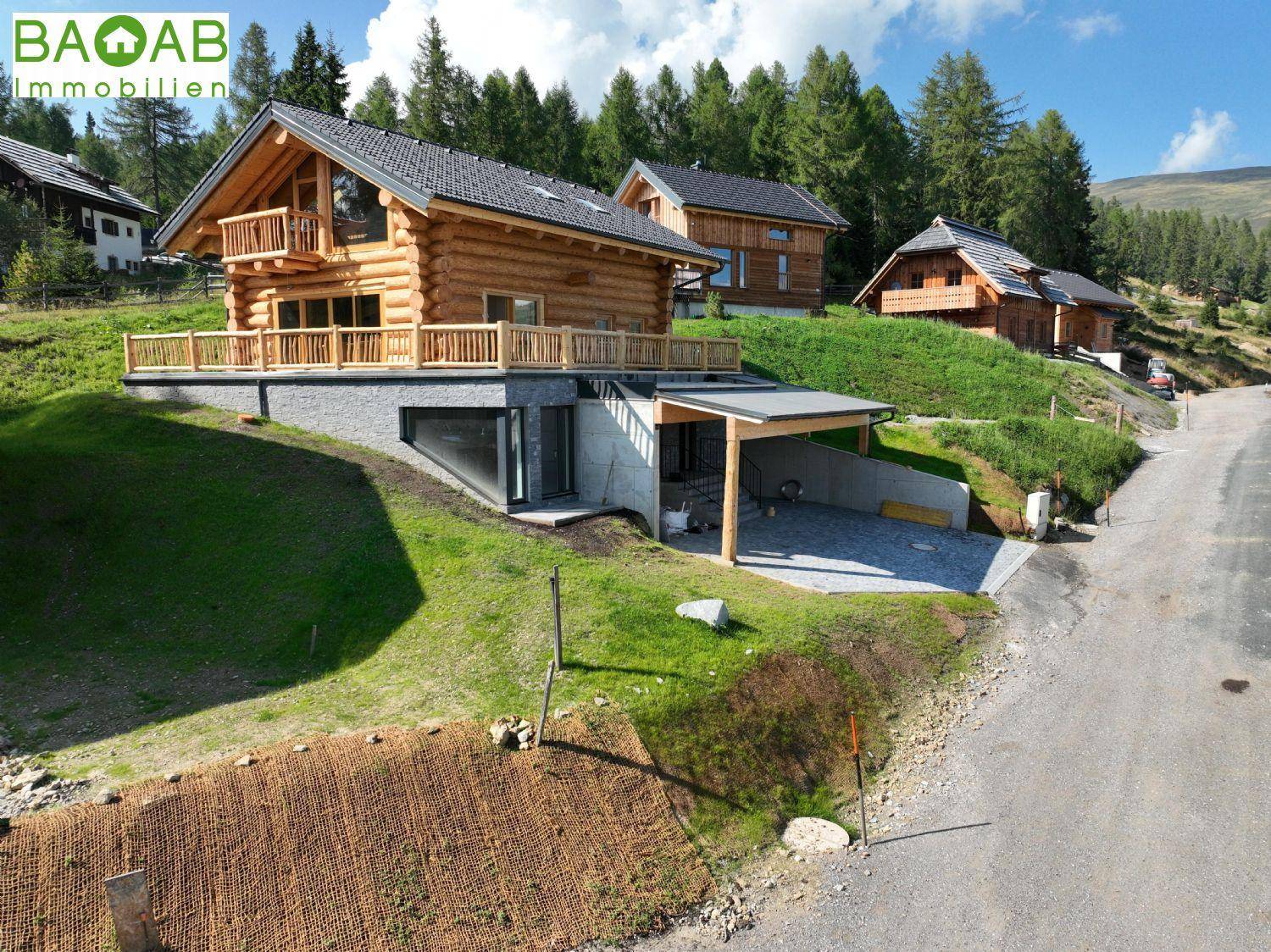 Mehrere Holzchalets auf einem Hanggrundstück mit Carport und Zufahrtsstraße in den Bergen.