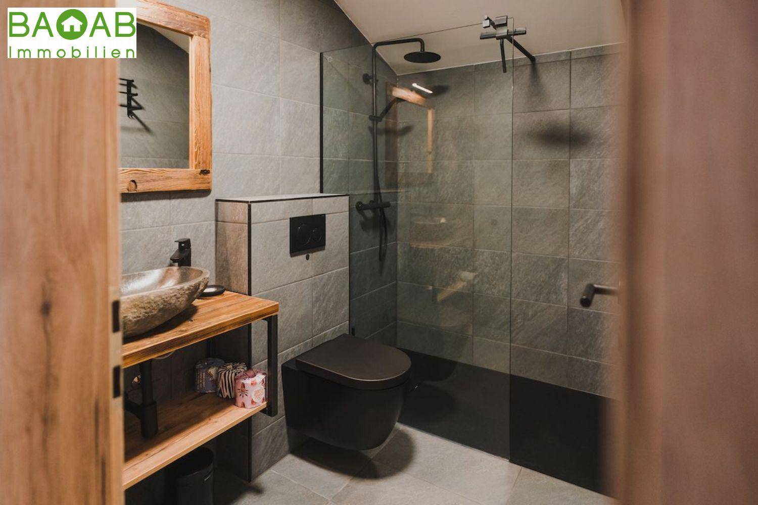Modernes Badezimmer mit grauen Fliesen, begehbarer Dusche und einem Natursteinwaschbecken.
