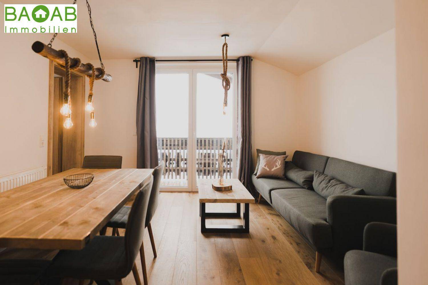 Helles Wohn- und Esszimmer mit Holztisch, Sofa und Zugang zu einem Balkon.