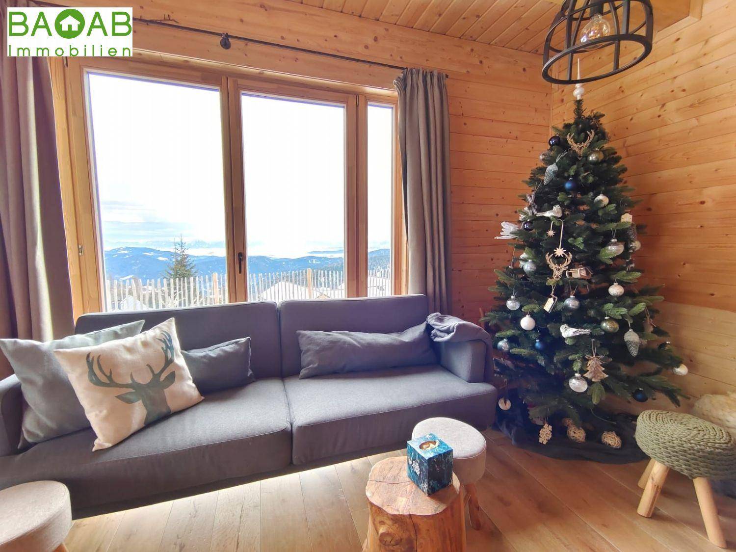 Gemütliches Wohnzimmer mit Holzwänden, Sofa und Panoramablick auf die verschneiten Berge.