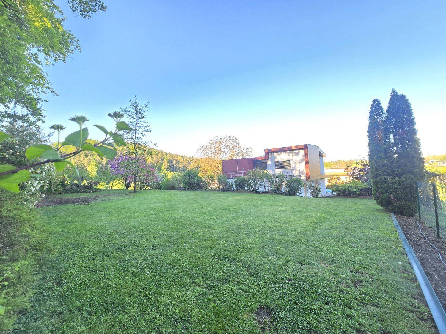 Großer, gepflegter Rasenbereich mit moderner Villa im Hintergrund unter blauem Himmel.