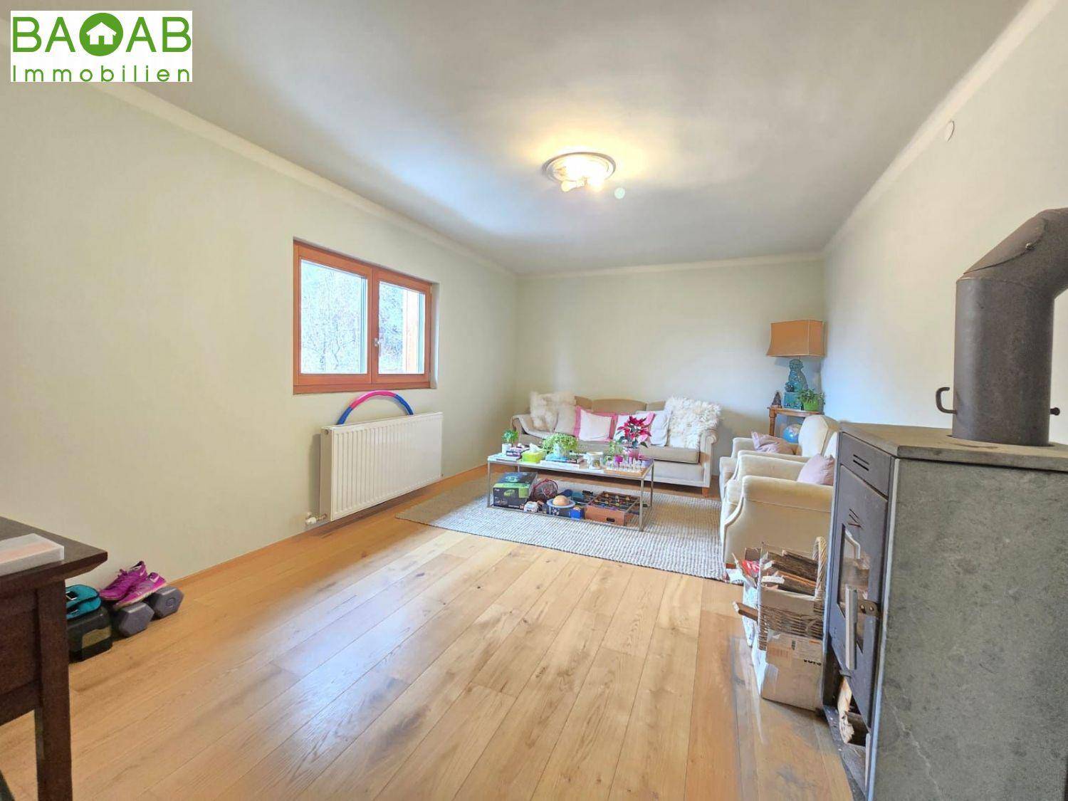 Wohnzimmer mit Holzboden, Sofa und einem traditionellen Holzofen für gemütliche Wärme.