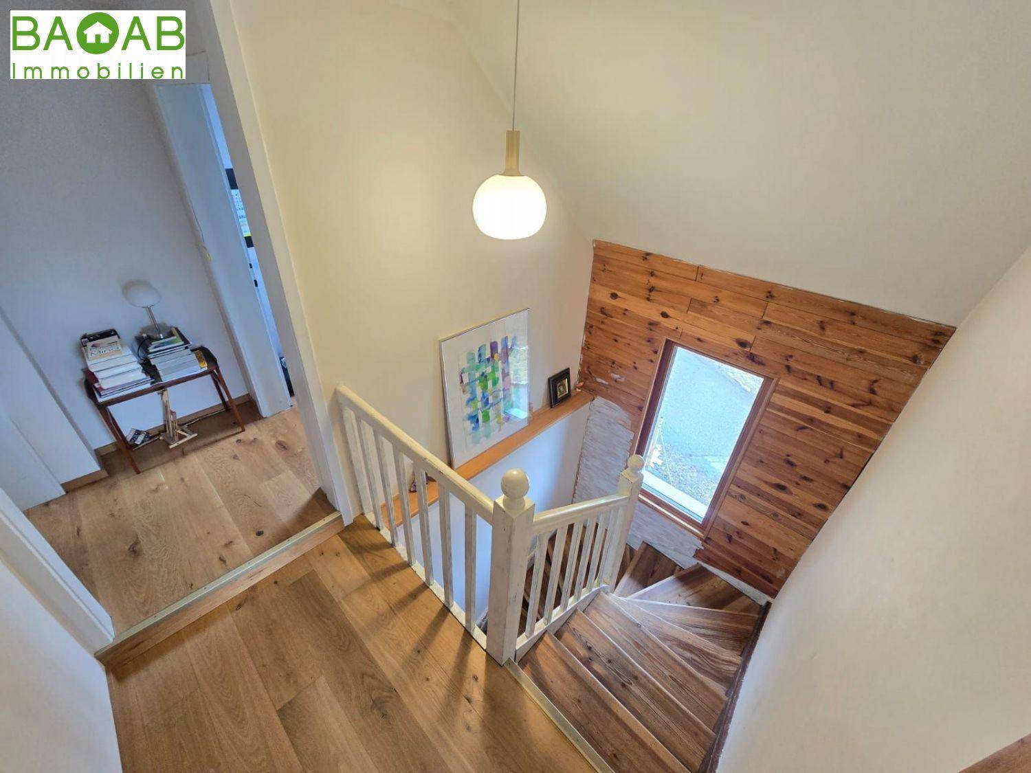 Holztreppe mit weißem Geländer und Holzwandverkleidung, die verschiedene Ebenen verbindet.