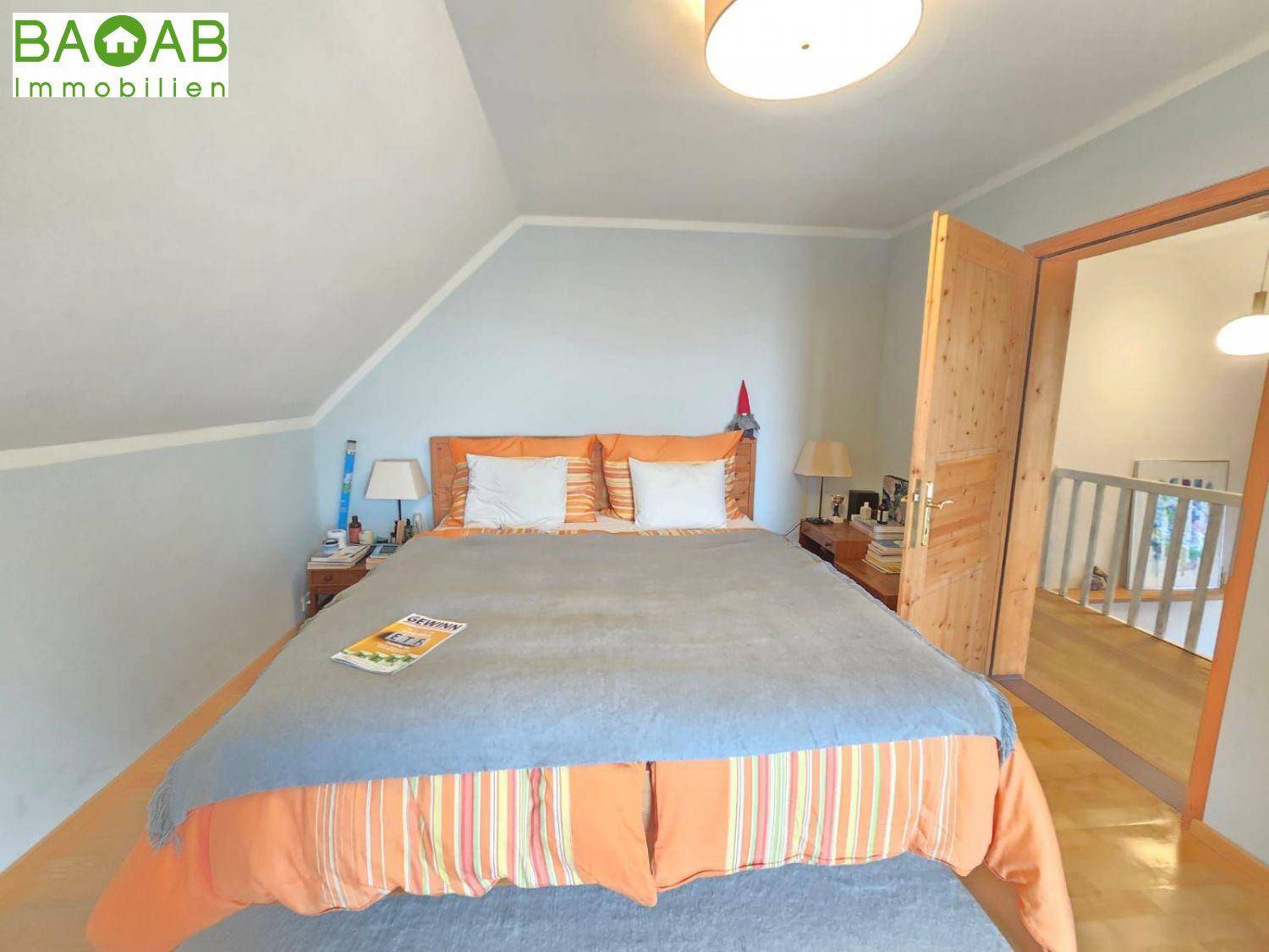 Schlafzimmer mit Dachschräge, Holzboden und Zugang zu einem weiteren Raum.