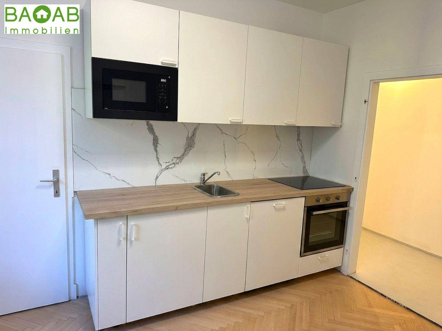 Kleine moderne Küche mit weißen Schränken, Holzarbeitsplatte und integrierten Geräten.