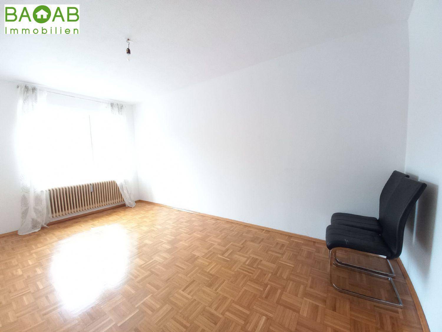 Heller Raum mit Fischgrätparkett und einem Heizkörper unter dem Fenster, bereit zur Einrichtung.