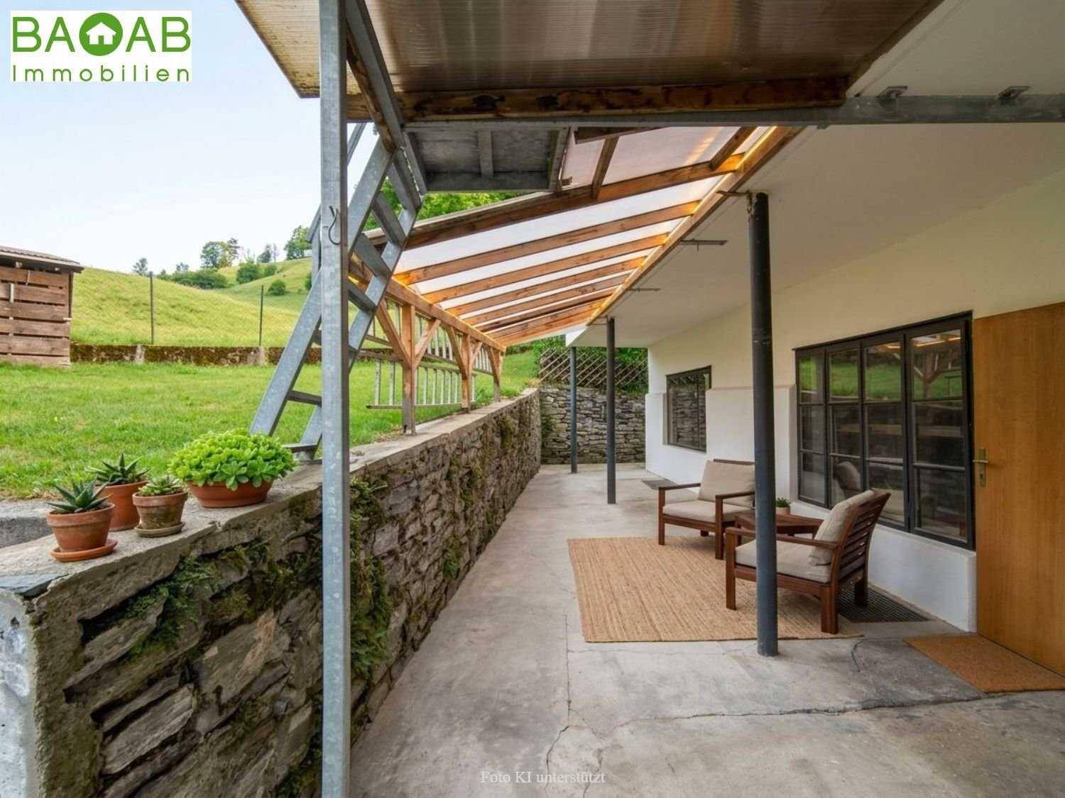 Überdachter Außenbereich mit rustikaler Steinmauer und Blick auf die grüne Landschaft, ideal zum Entspannen.
