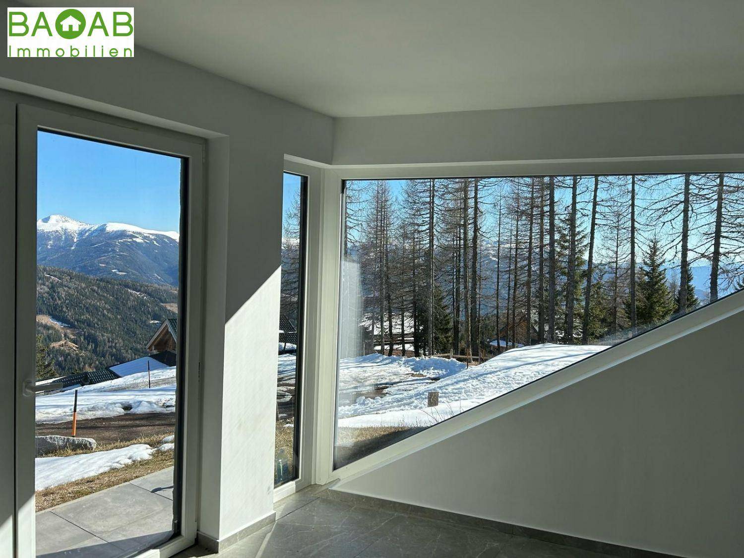 Heller Raum mit großen, modernen Fenstern und weitem Blick auf verschneite Berge und Wälder.