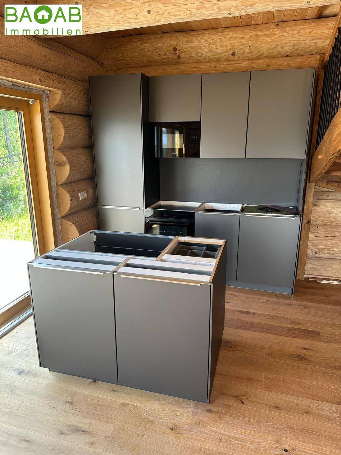 Moderne Küche im Aufbau mit grauen Schränken, Kücheninsel und rustikalen Holzwänden.
