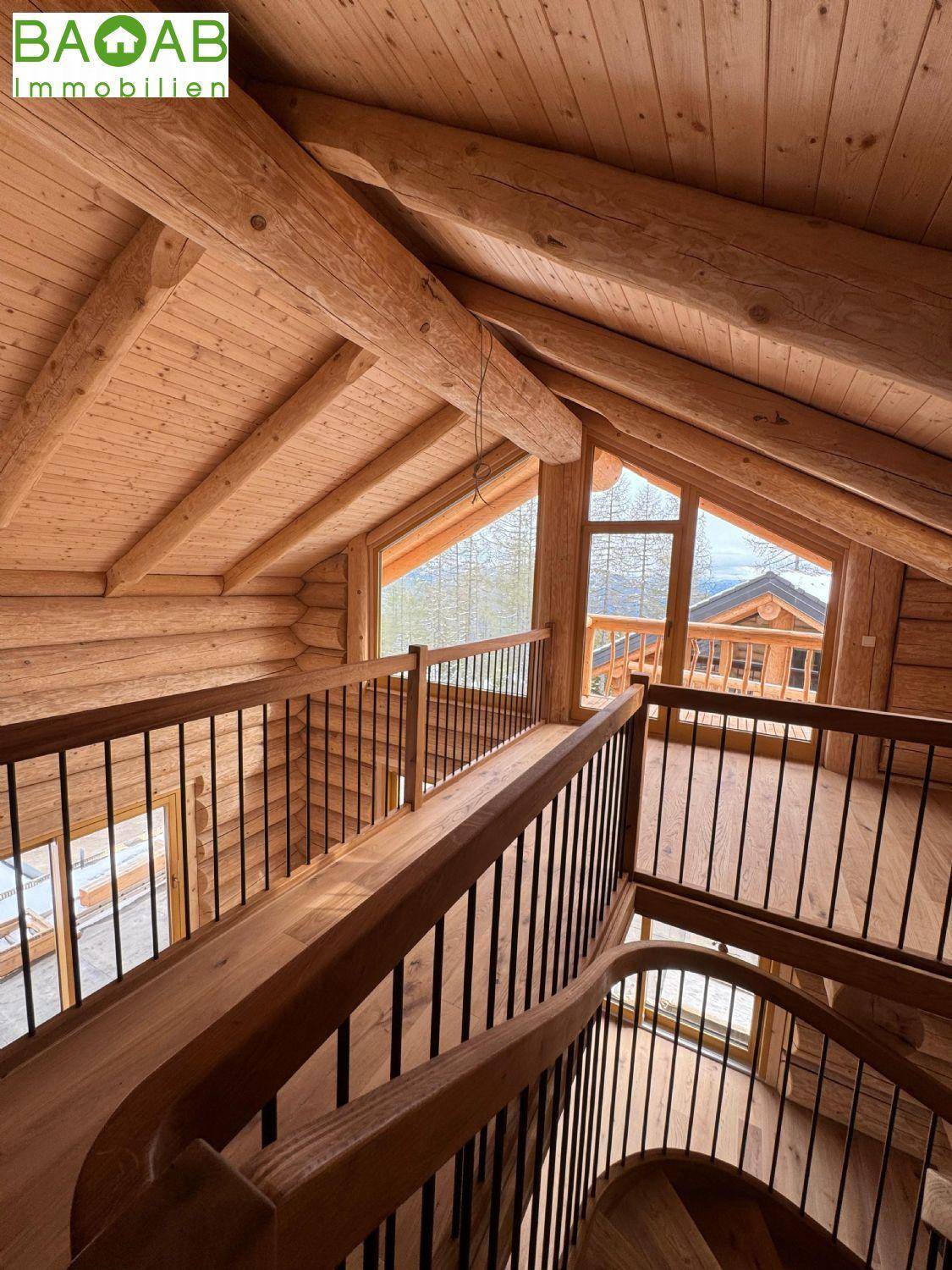 Geschwungene Holztreppe mit Metallgeländer in einem Haus mit sichtbaren Holzbalken und Dachschrägen.