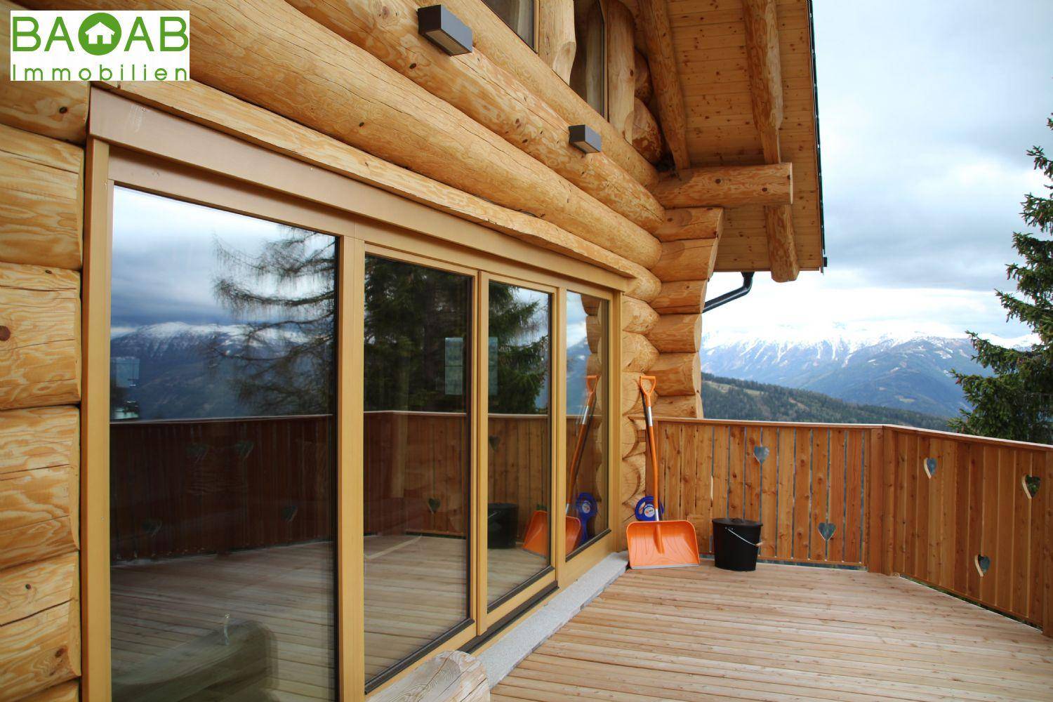 Holzhaus mit großem Balkon und Schiebetüren, der einen weiten Blick auf die verschneite Berglandschaft bietet.