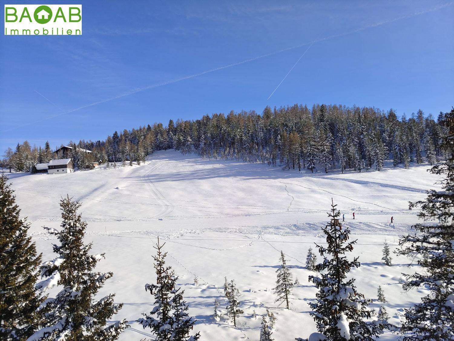 Idyllische, schneebedeckte Landschaft mit weiten Feldern, Wäldern und einem Haus in der Ferne.