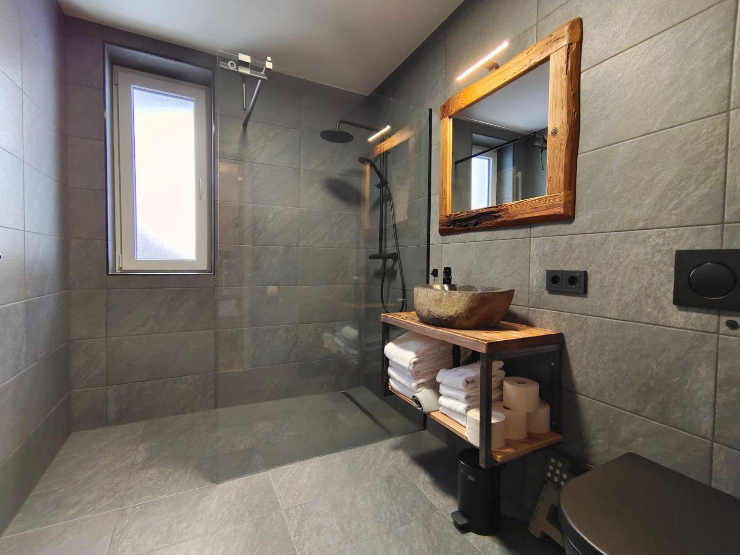 Stilvolles Badezimmer mit begehbarer Dusche, grauen Fliesen und rustikalem Waschtisch.