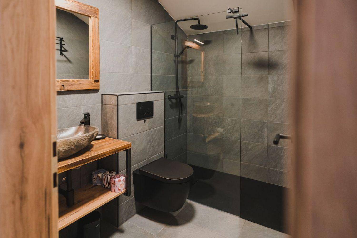 Modernes Badezimmer mit dunkler Toilette, begehbarer Dusche und einzigartigem Steinwaschbecken.