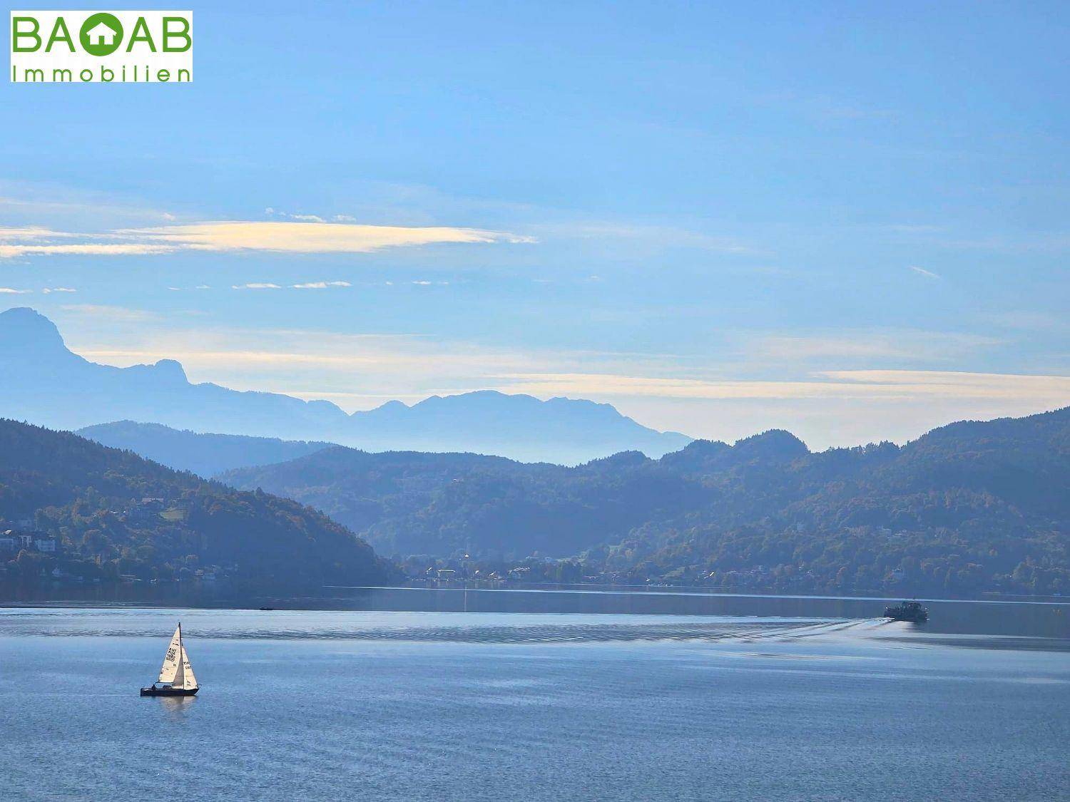 Malerischer Blick auf einen ruhigen See mit Segelboot und majestätischen Bergen im Hintergrund.